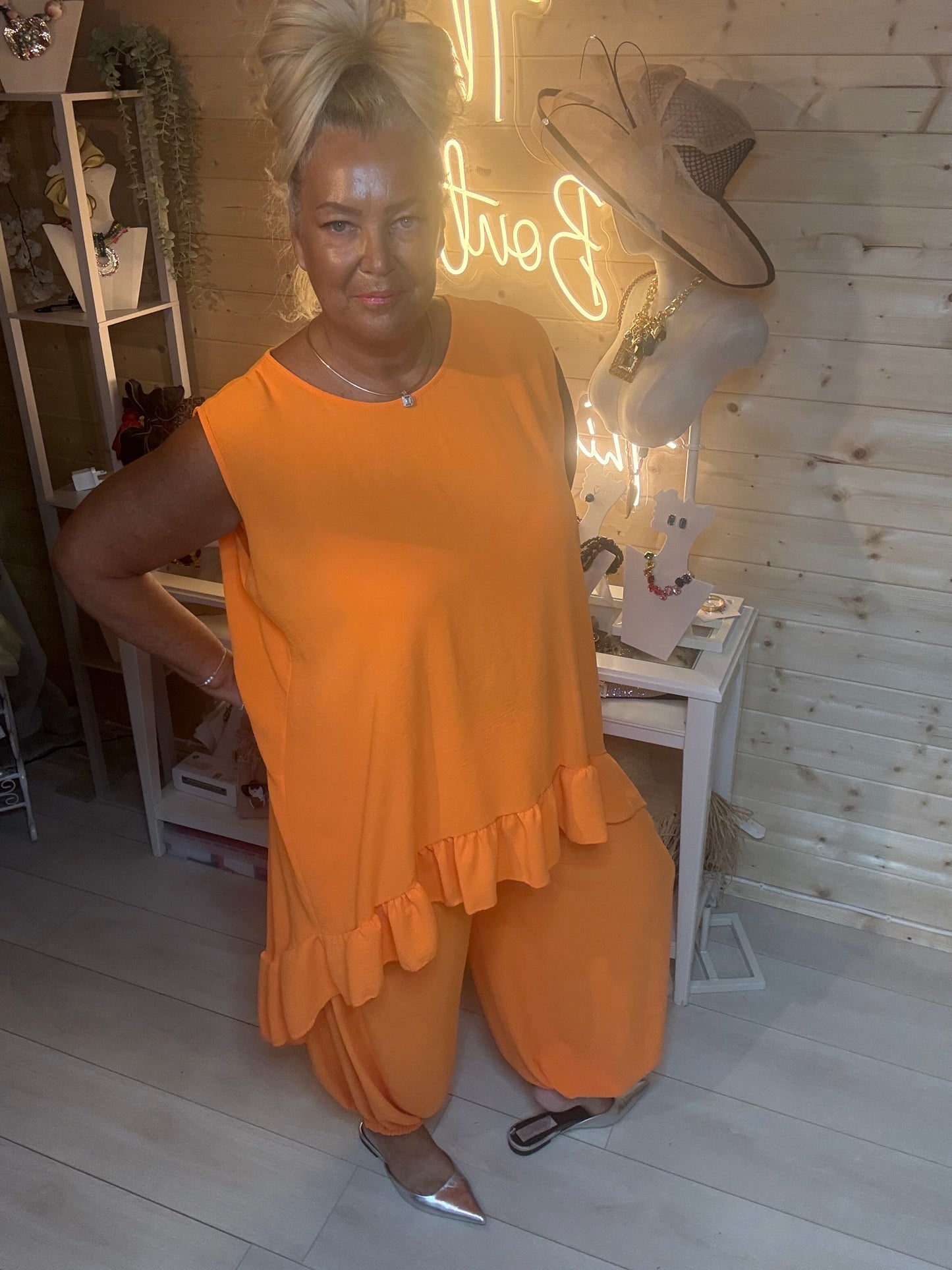 Orange co-ord set – three quarter length boutique shot showing full silhouette of ruffle hem top and harem trousers with silver mules