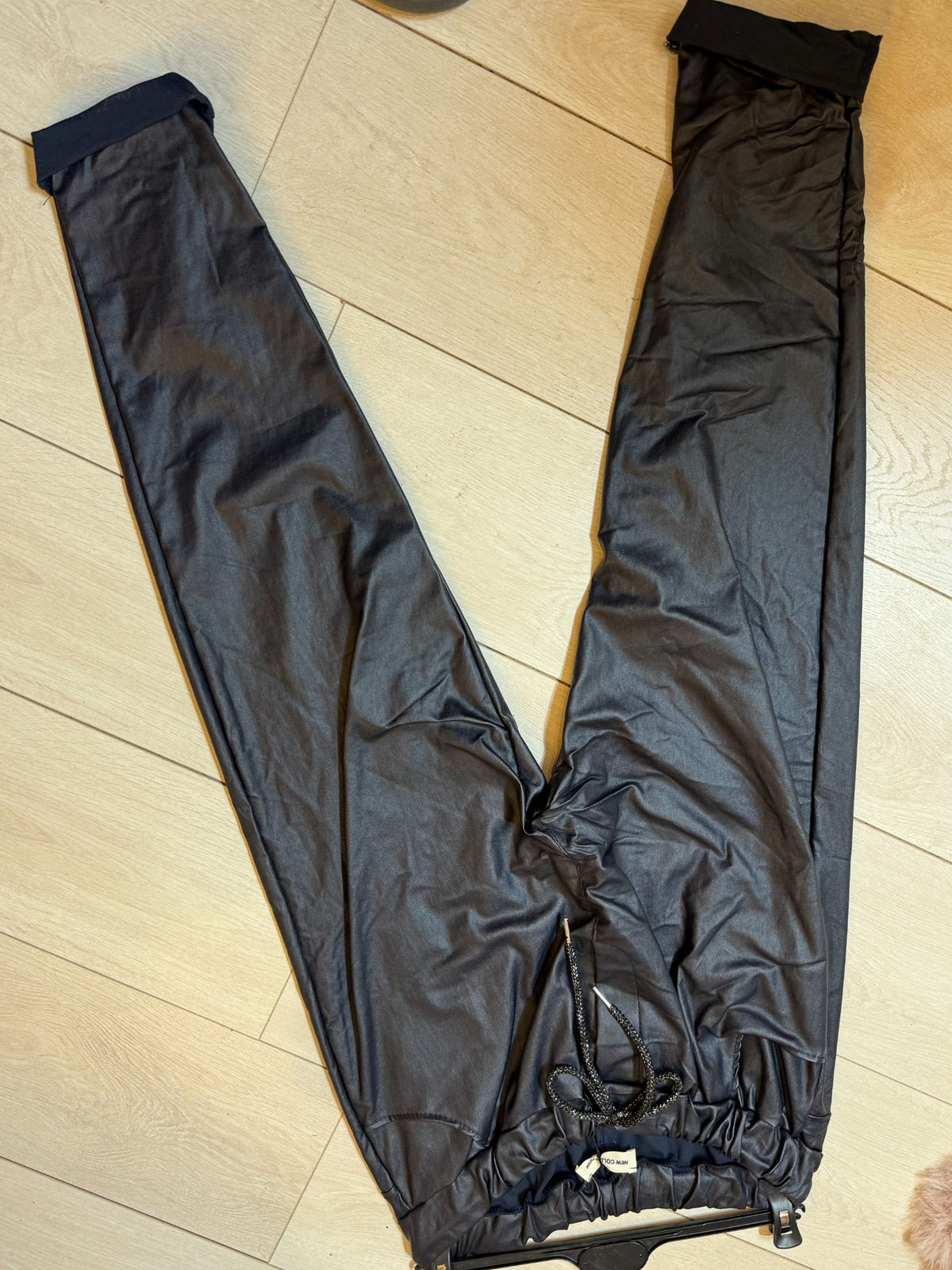 Black PU coated magic trousers with drawstring waist and cuffed hems laid flat