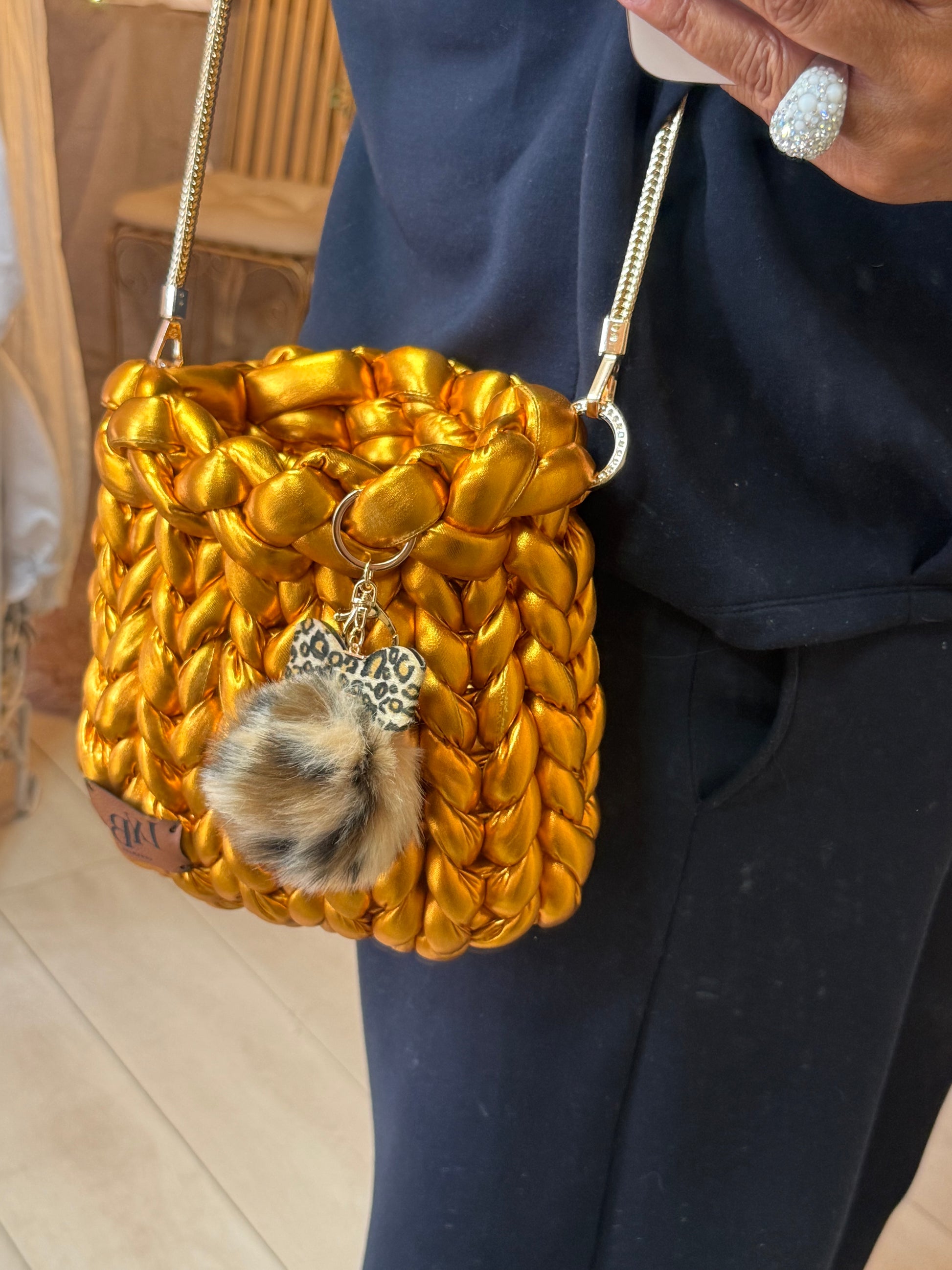 Gold rush metallic chunky braid bucket bag worn crossbody over navy outfit with gold chain strap