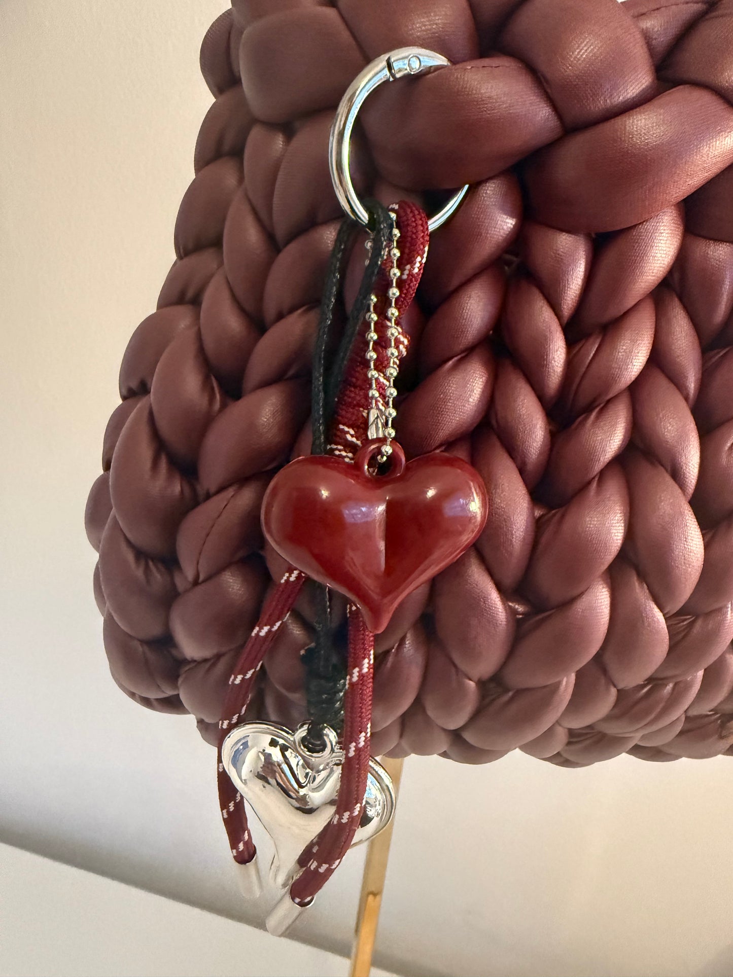Close-up of red ceramic heart and silver open heart charm on Bordeaux braided bag