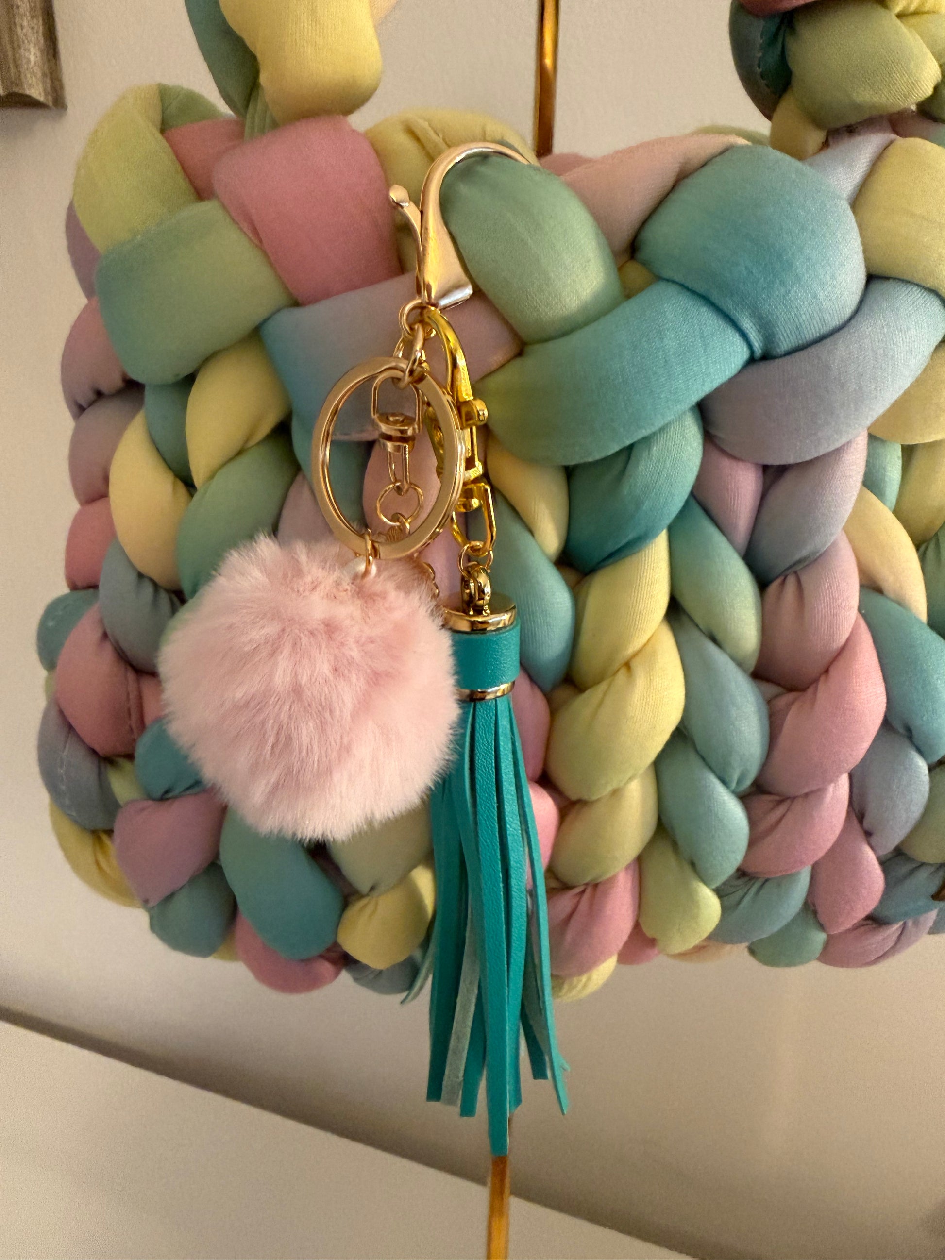Close-up of fluffy blush pom pom and teal leather tassel charm on Candy braided bag with gold hardware