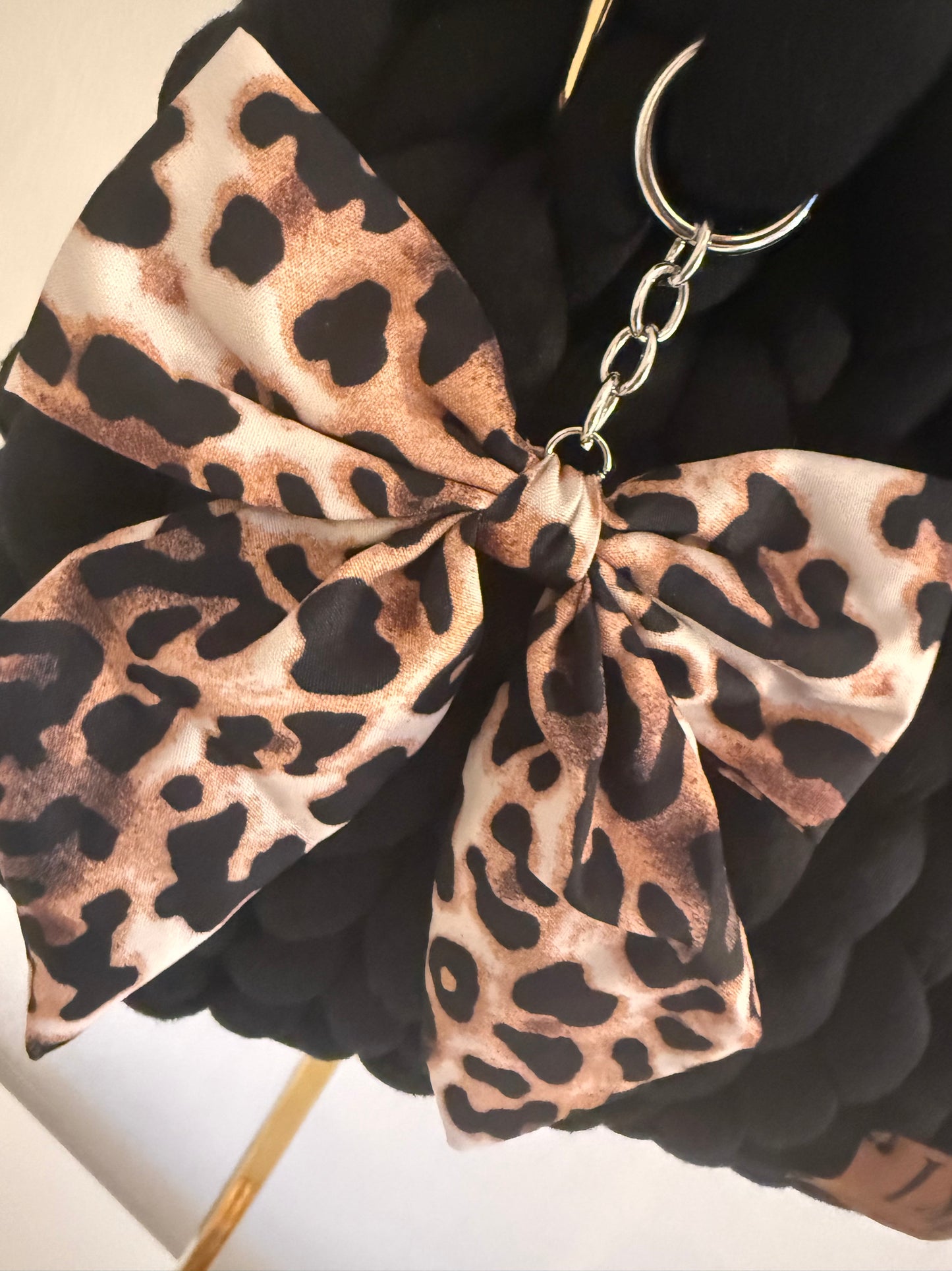 Close-up of detachable oversized leopard print satin bow charm on silver keyring on Chloe black bag