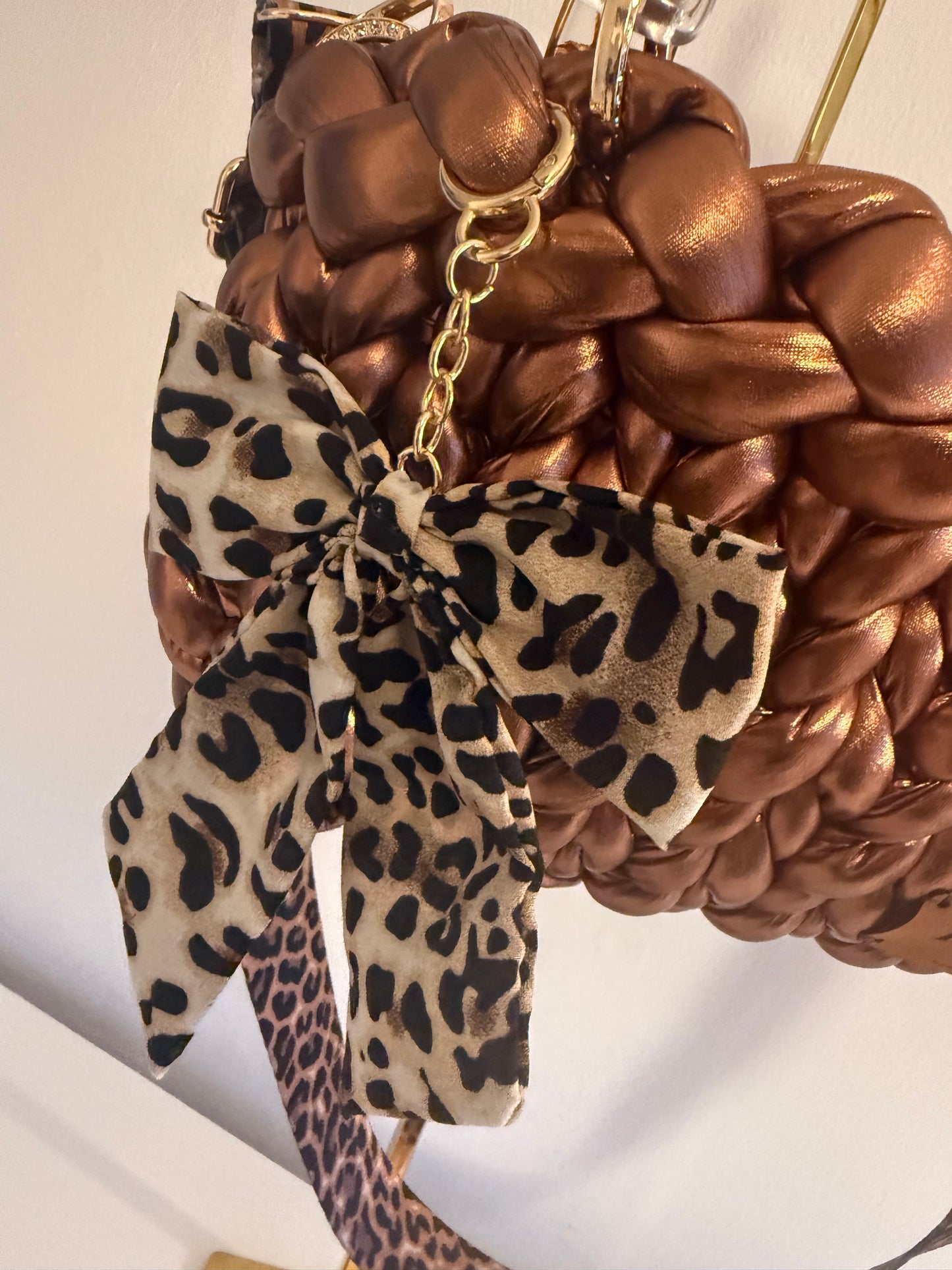 Close-up of detachable leopard print bow charm on gold chain on Rustica bronze bag