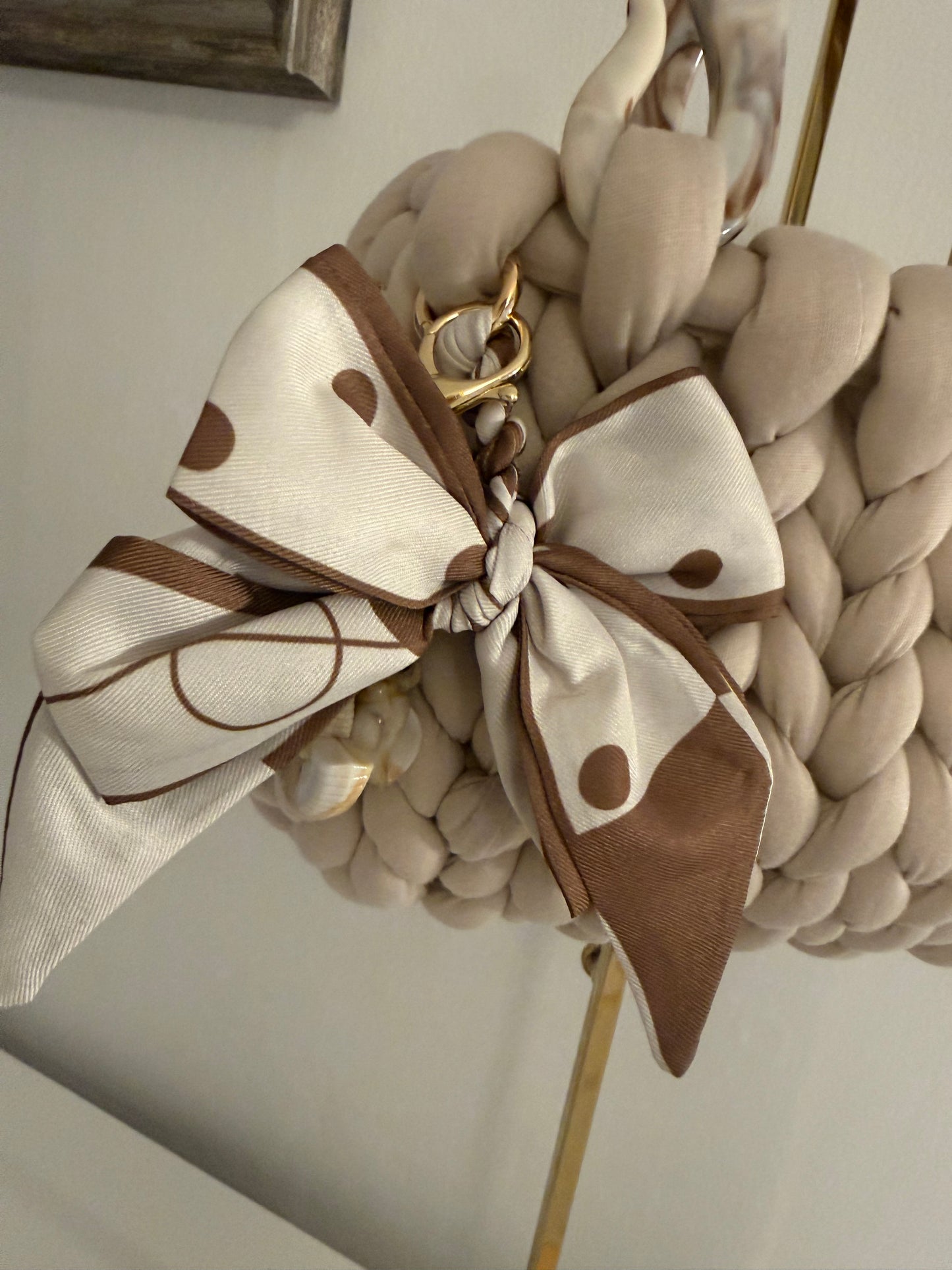 Close-up of detachable cream and chocolate polka dot satin bow charm with gold clasp on Latte bag