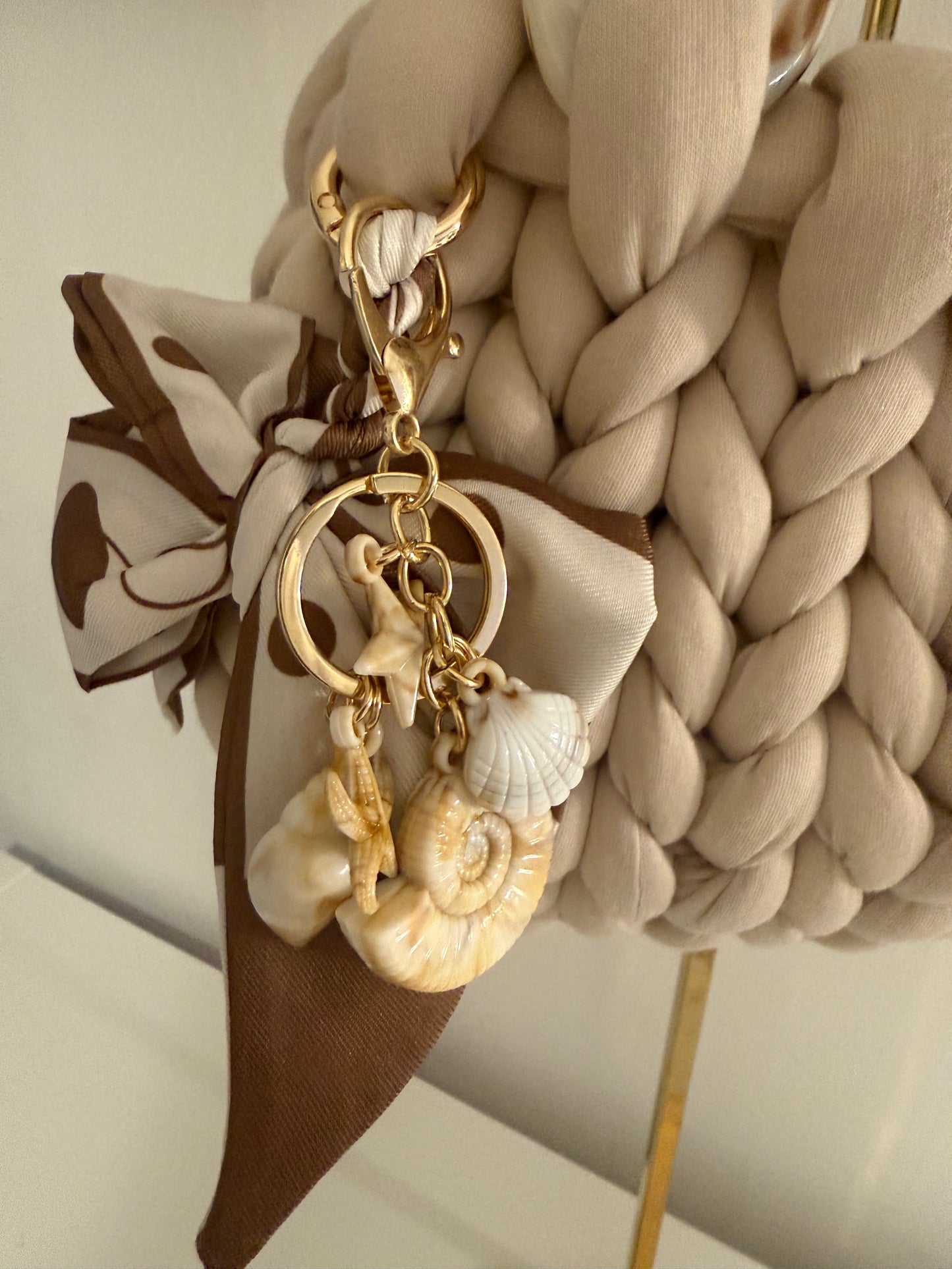 Close-up of detachable seashell and starfish charm cluster on gold chain on Latte cream bag