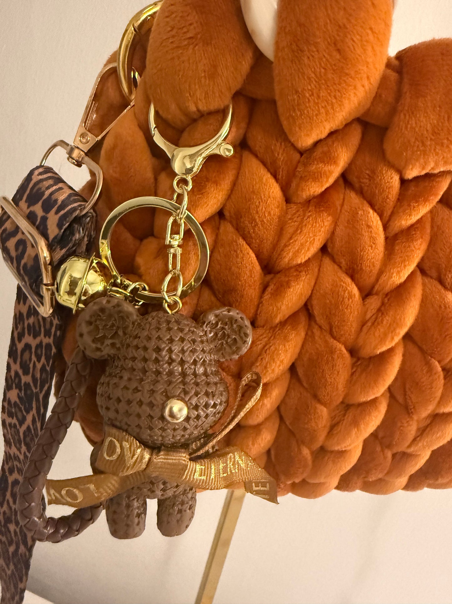 Close-up of detachable woven teddy bear charm with gold ribbon bow and gold-tone lobster clasp on Autumn Lust bag