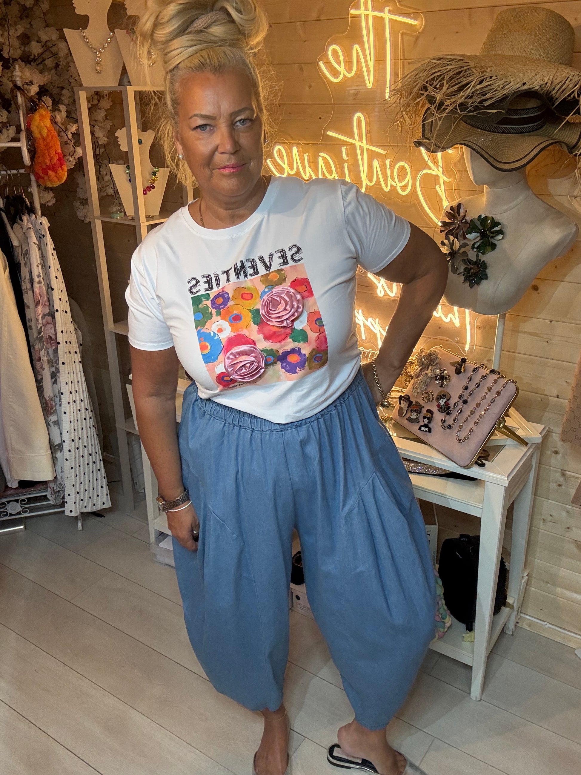 Woman wearing Seventies slogan tee with pop-art floral print and 3D roses – boutique front view with denim harem trousers