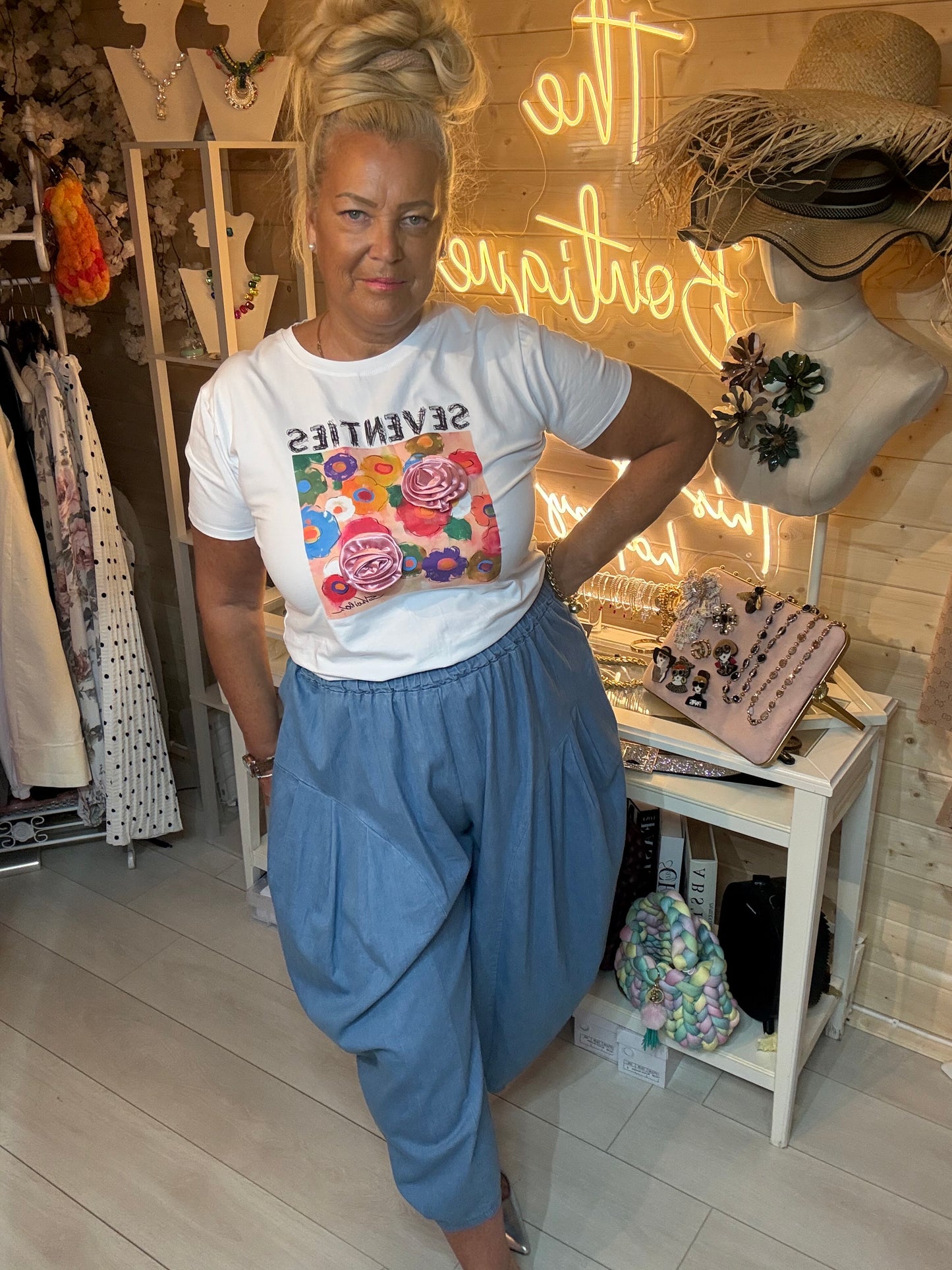 Woman wearing Seventies white graphic t-shirt with 3D rose appliqué and denim harem trousers – boutique front view