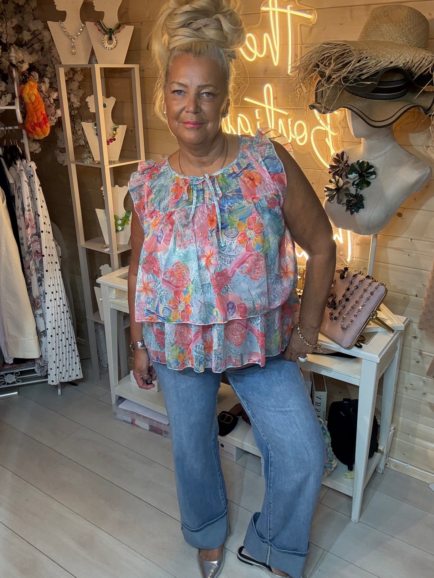 Woman wearing Flora floral ruffle chiffon top with blue jeans in boutique – front view