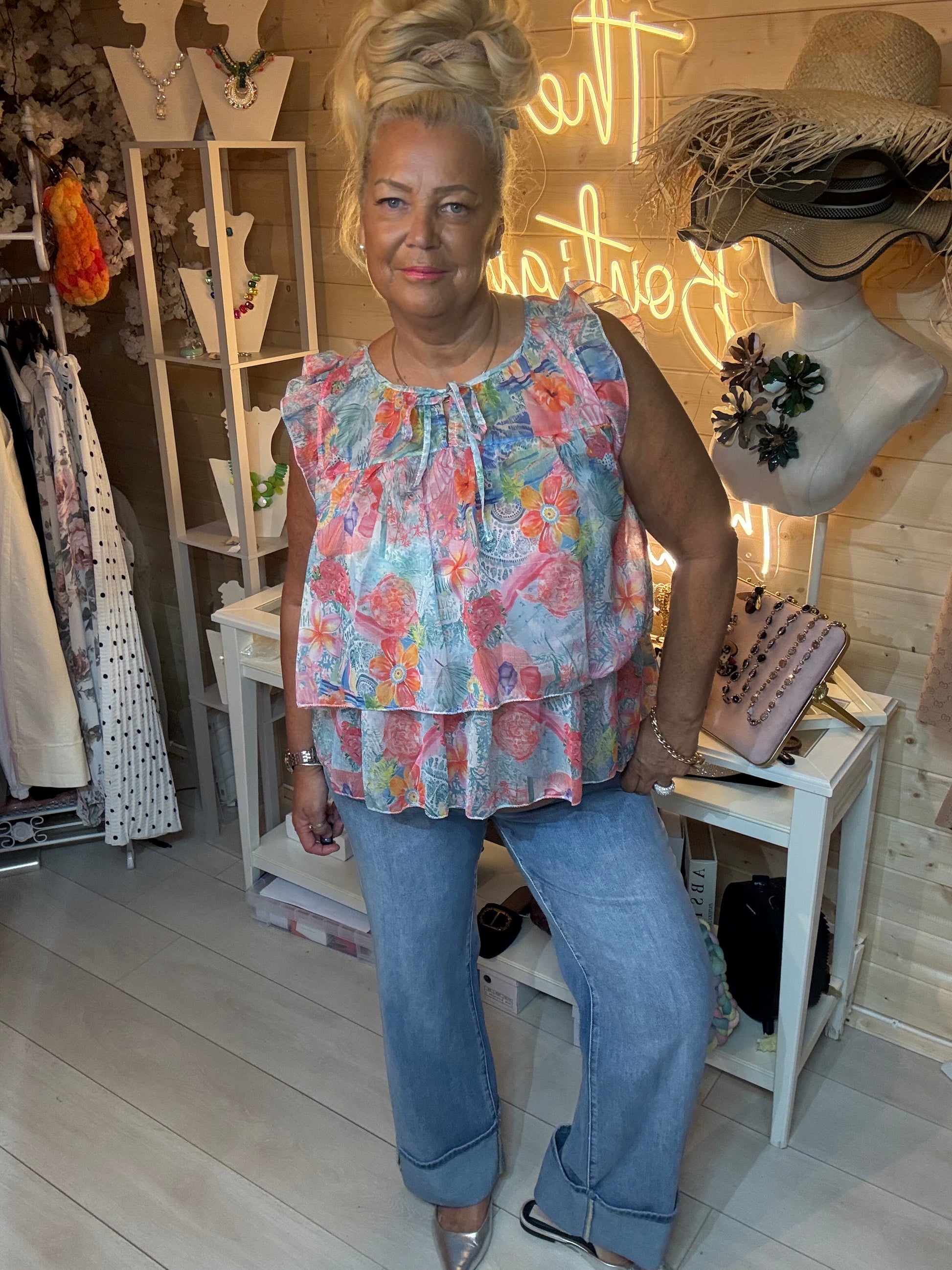 Woman wearing Flora floral ruffle chiffon top with blue jeans in boutique – front view