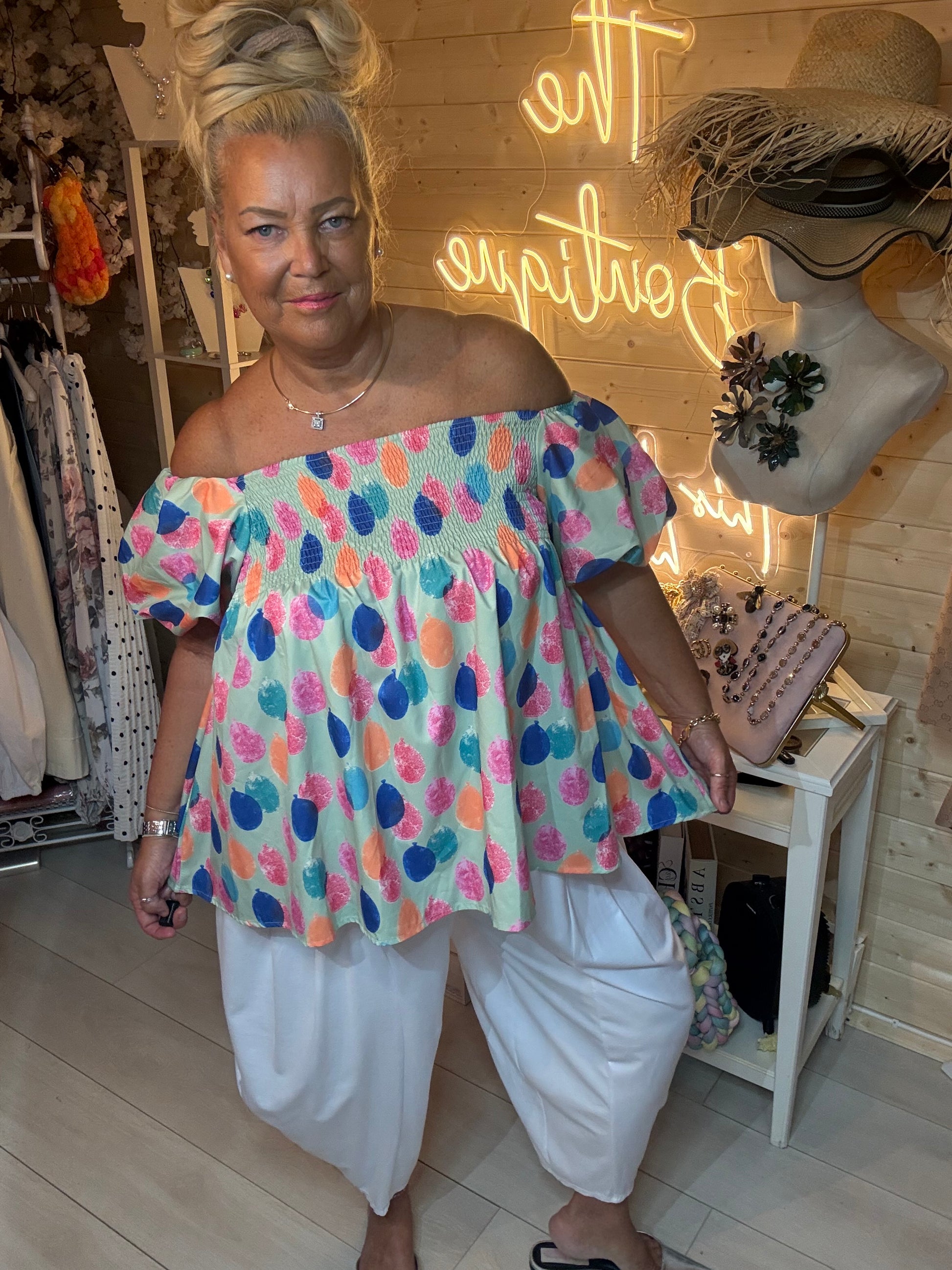 Sorbet bardot top with multicolour fruit-dot print styled with white trousers – full length view