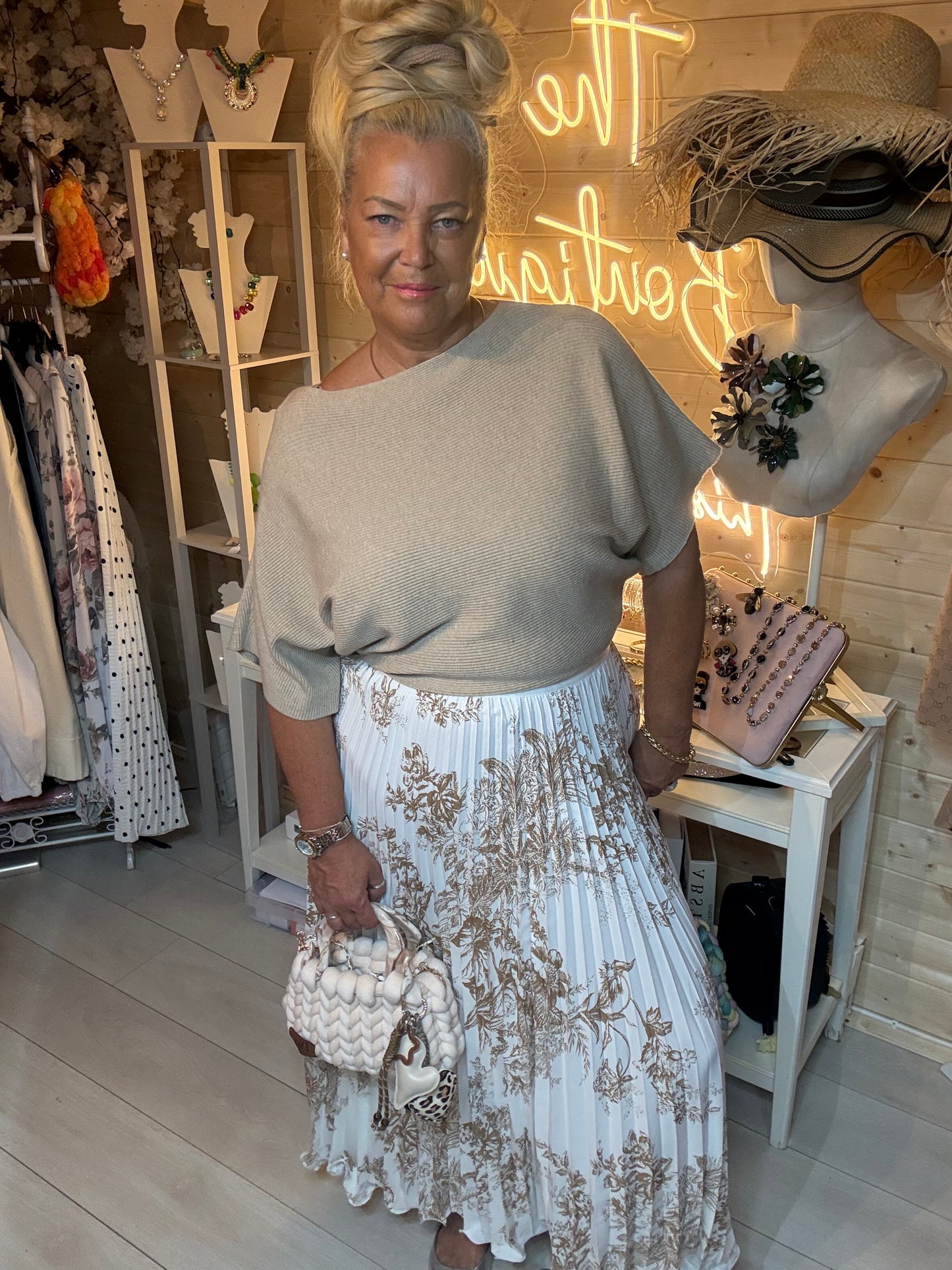 Woman wearing Oatmeal batwing knit top with gold floral pleated midi skirt – boutique front view