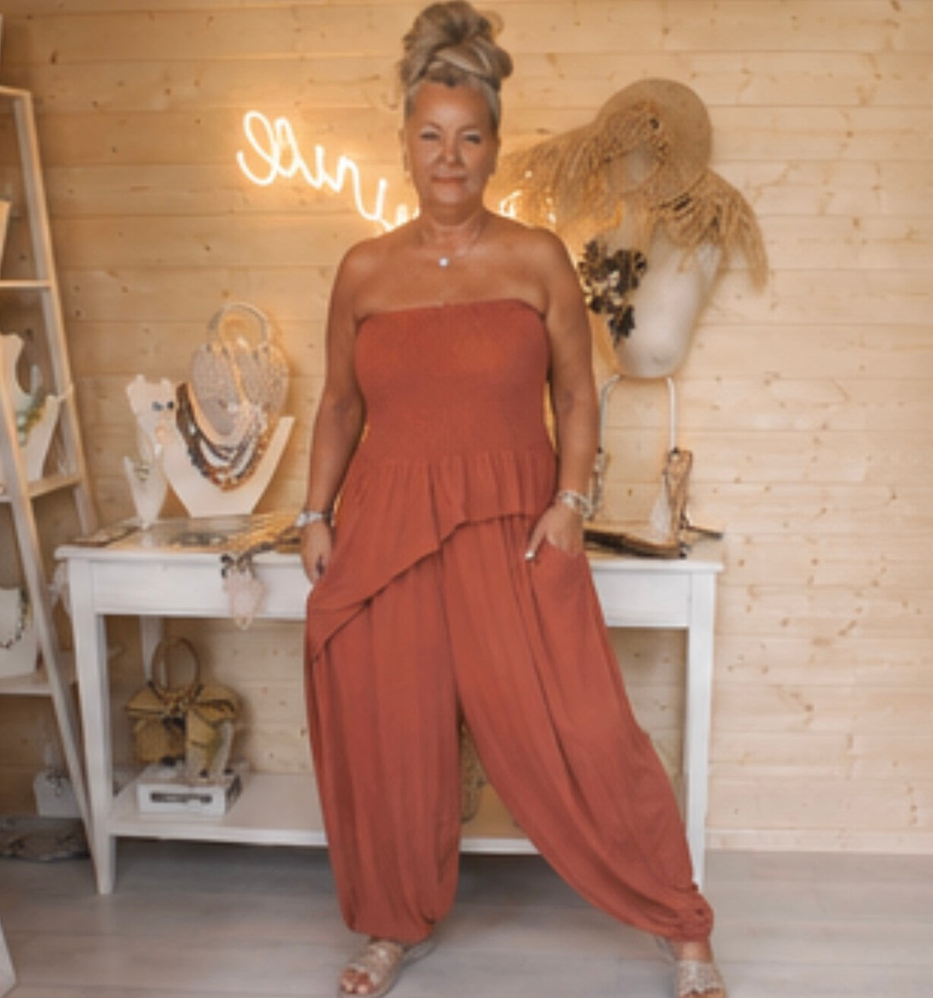 Woman wearing Riviera terracotta strapless peplum jumpsuit with wide-leg harem trousers – boutique front view