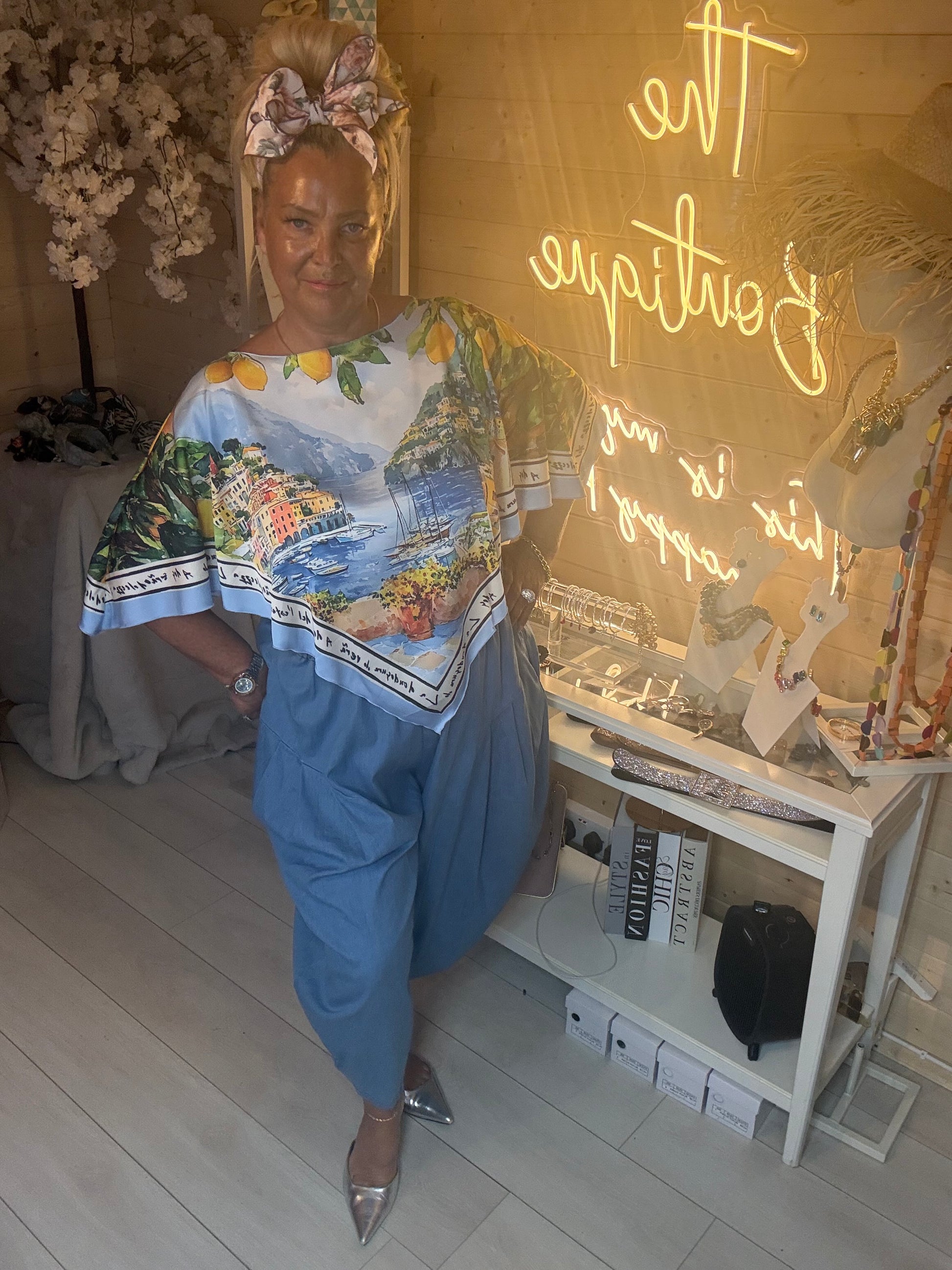 Woman wearing Amalfi Poncho Top with Italian coast print styled with light denim trousers in The Ultimate Ladies Boutique
