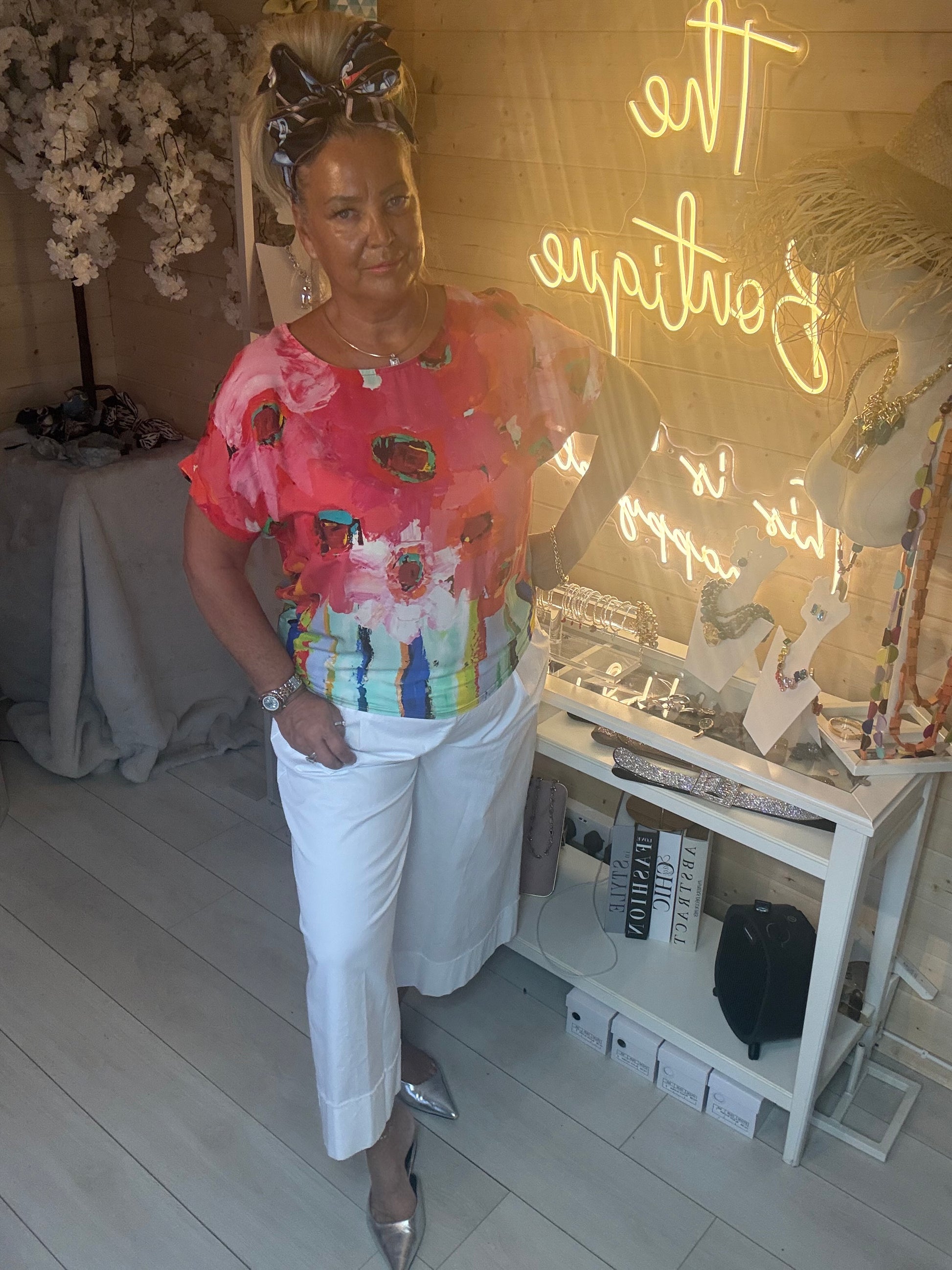 Woman wearing Sorento Coral Abstract Floral Poncho Top styled with white culottes and silver heels in The Ultimate Ladies Boutique