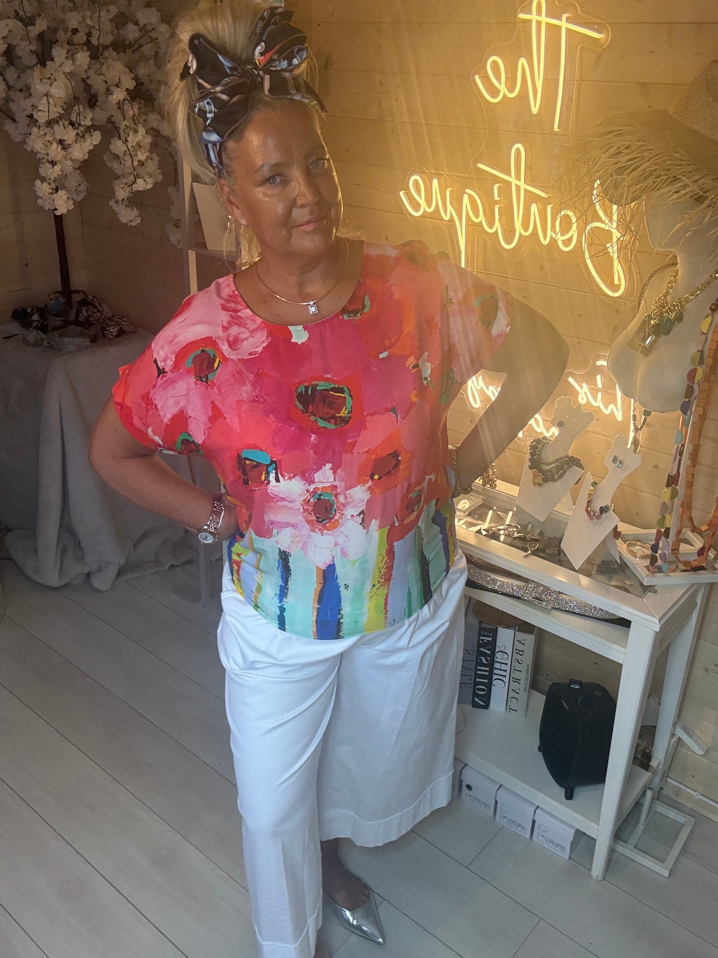 Close up of model smiling wearing Sorento Coral Abstract Floral Poncho Top with white culottes boutique background