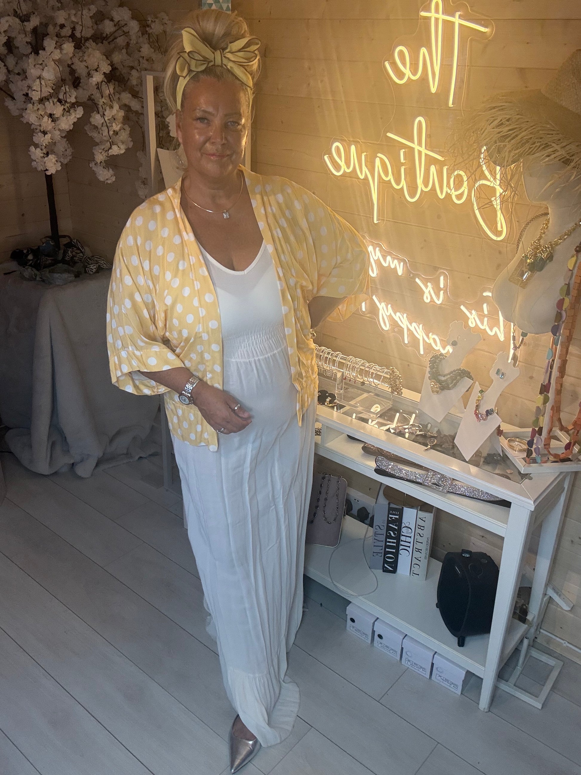 Woman wearing white ribbed maxi dress with yellow polka dot shawl draped over arm in The Ultimate Ladies Boutique