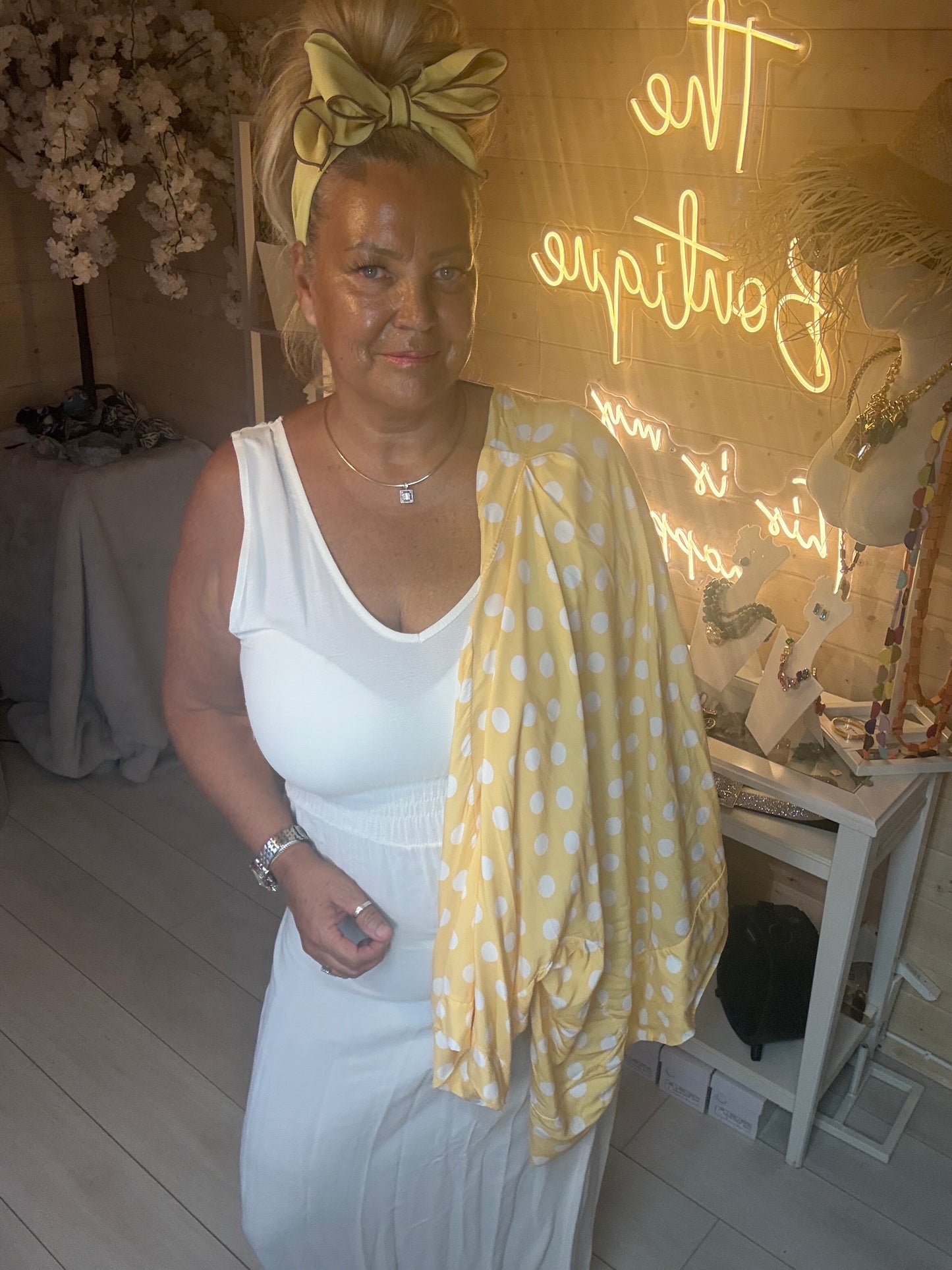 Close up of model wearing yellow polka dot kimono shawl jacket over white maxi dress holding white quilted bag