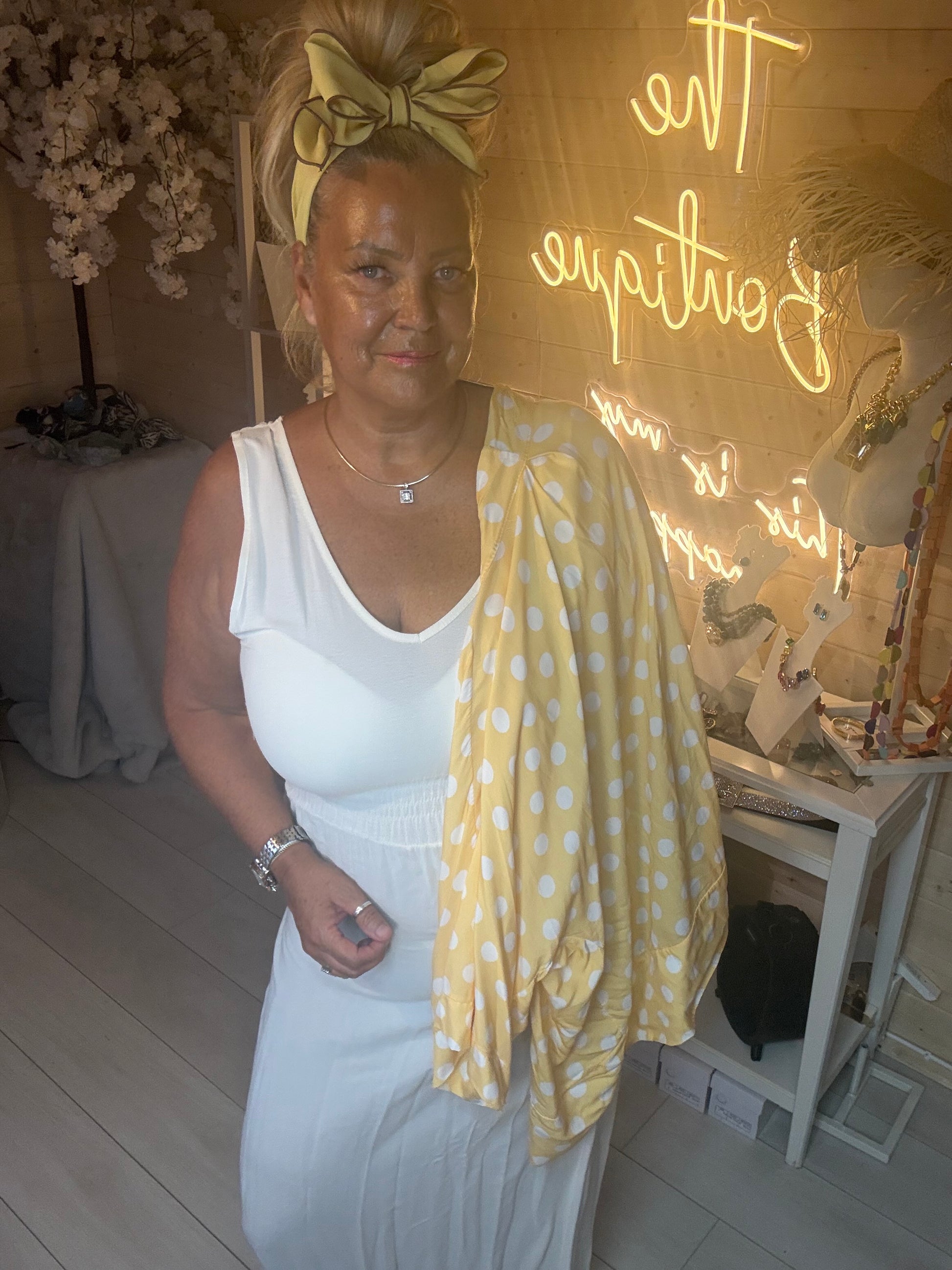 Close up of model wearing yellow polka dot kimono shawl jacket over white maxi dress holding white quilted bag