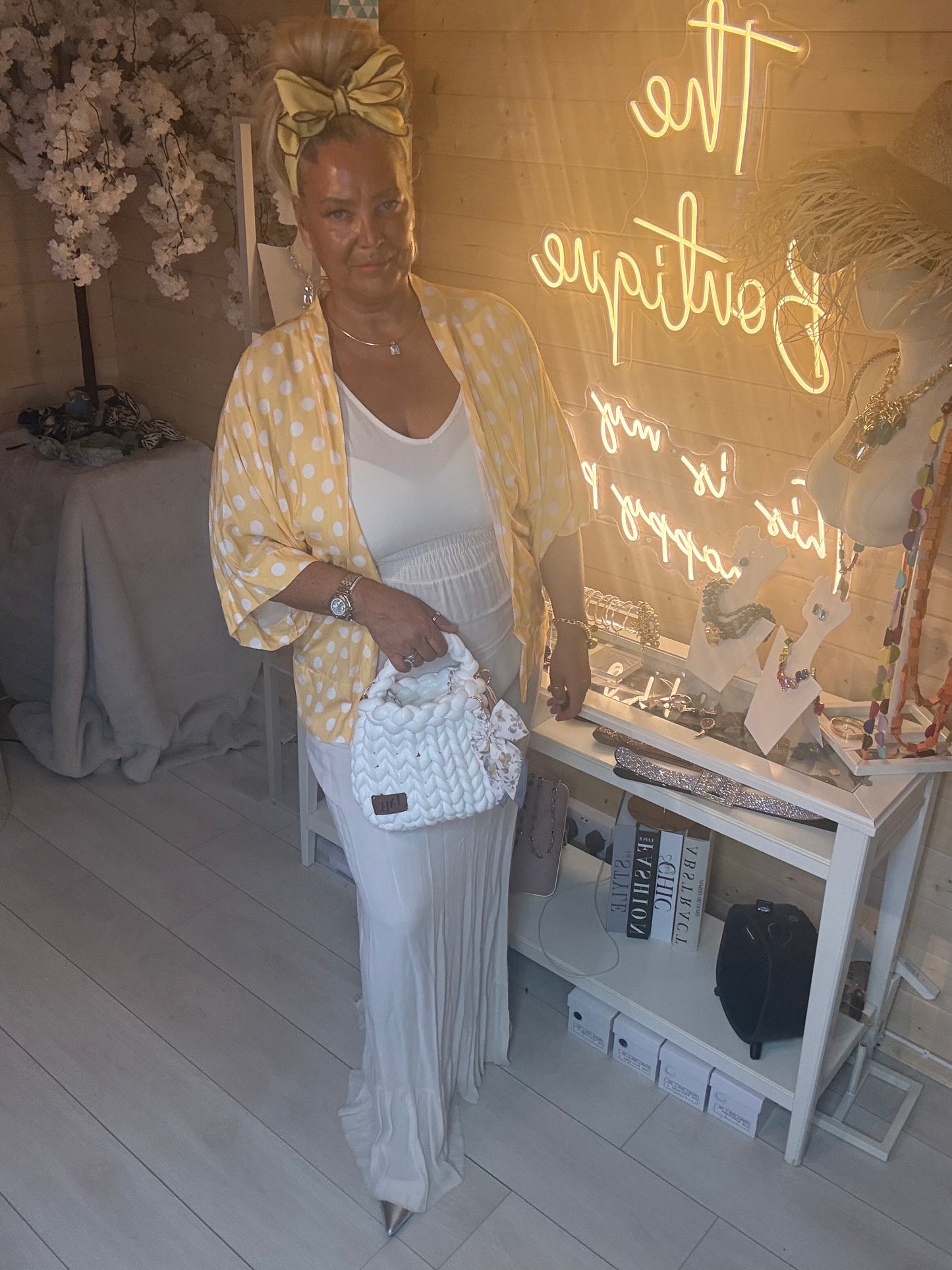 Model smiling wearing white ribbed maxi dress with yellow polka dot shawl draped showing tiered ruffle hem detail