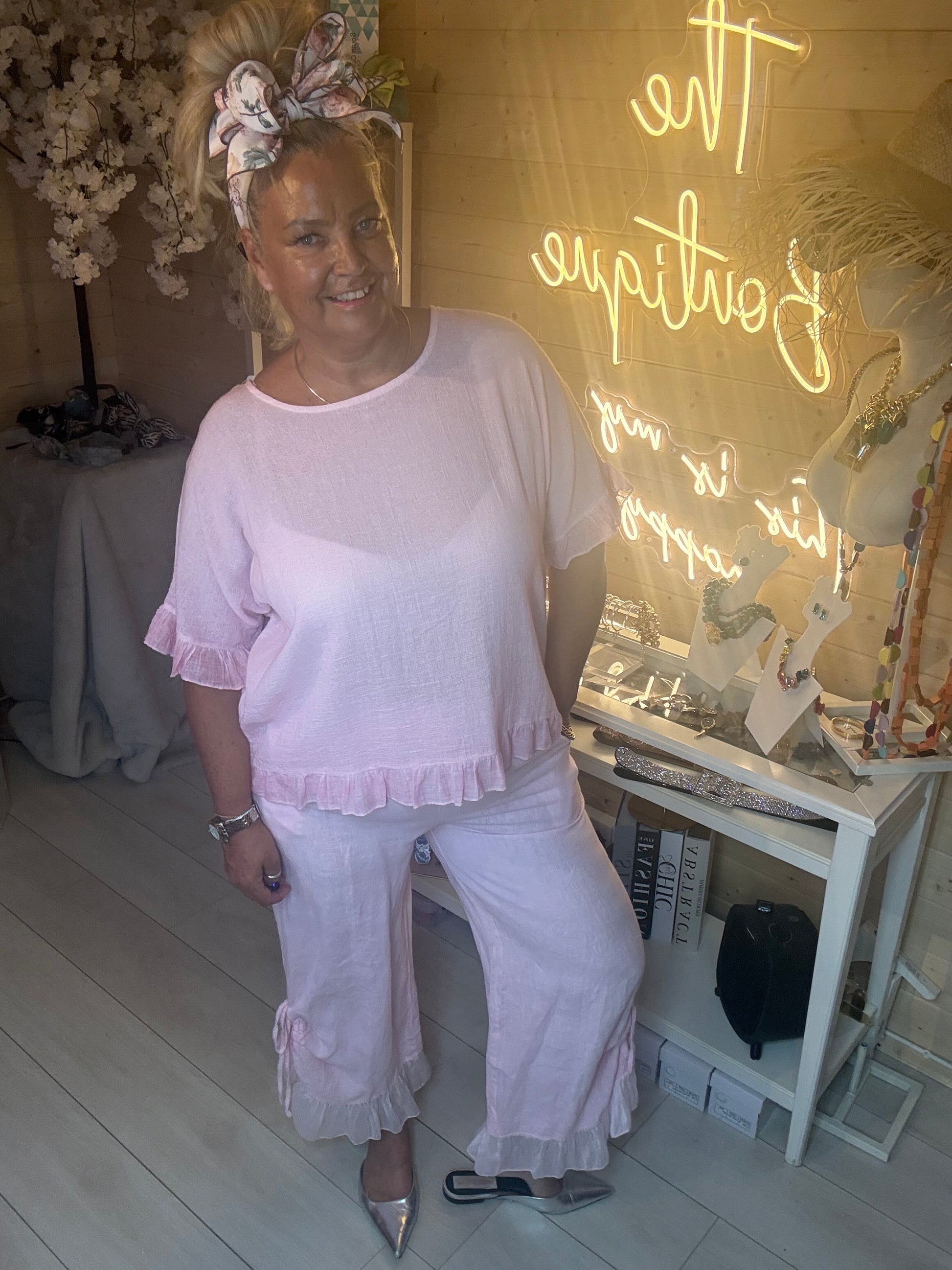 Woman wearing Rosa Blush Pink Ruffle Hem Crinkle Top with Sky Shimmer Ruffle Hem Linen Trousers in pink and silver heels in The Ultimate Ladies Boutique