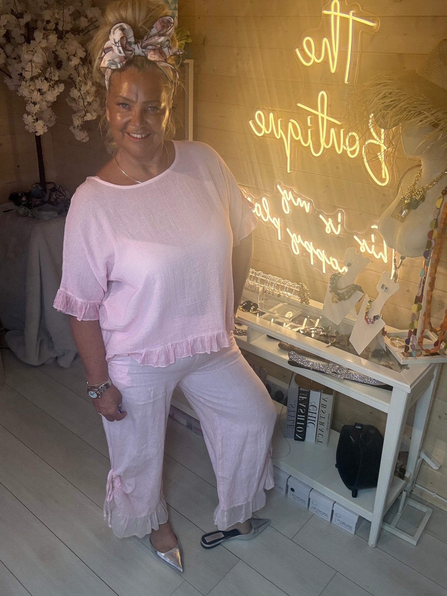 Seated pose of model in Rosa Blush Pink Ruffle Hem Crinkle Top and pink ruffle linen trousers showing relaxed co-ord outfit