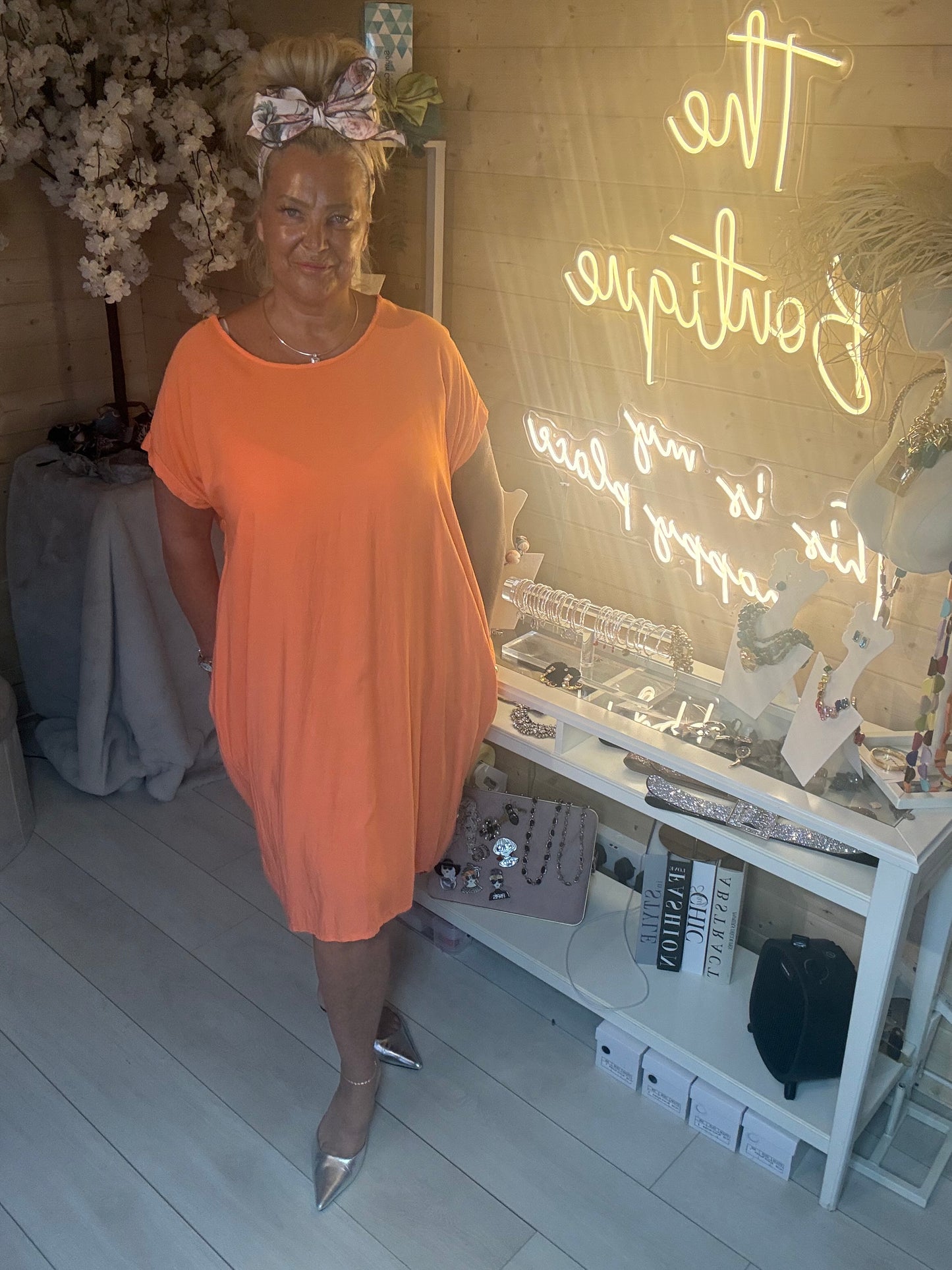 Full length view of Coral Cocoon Twist Back Jersey Dress with silver pointed heels showing knee length hem and relaxed fit one size 8-18