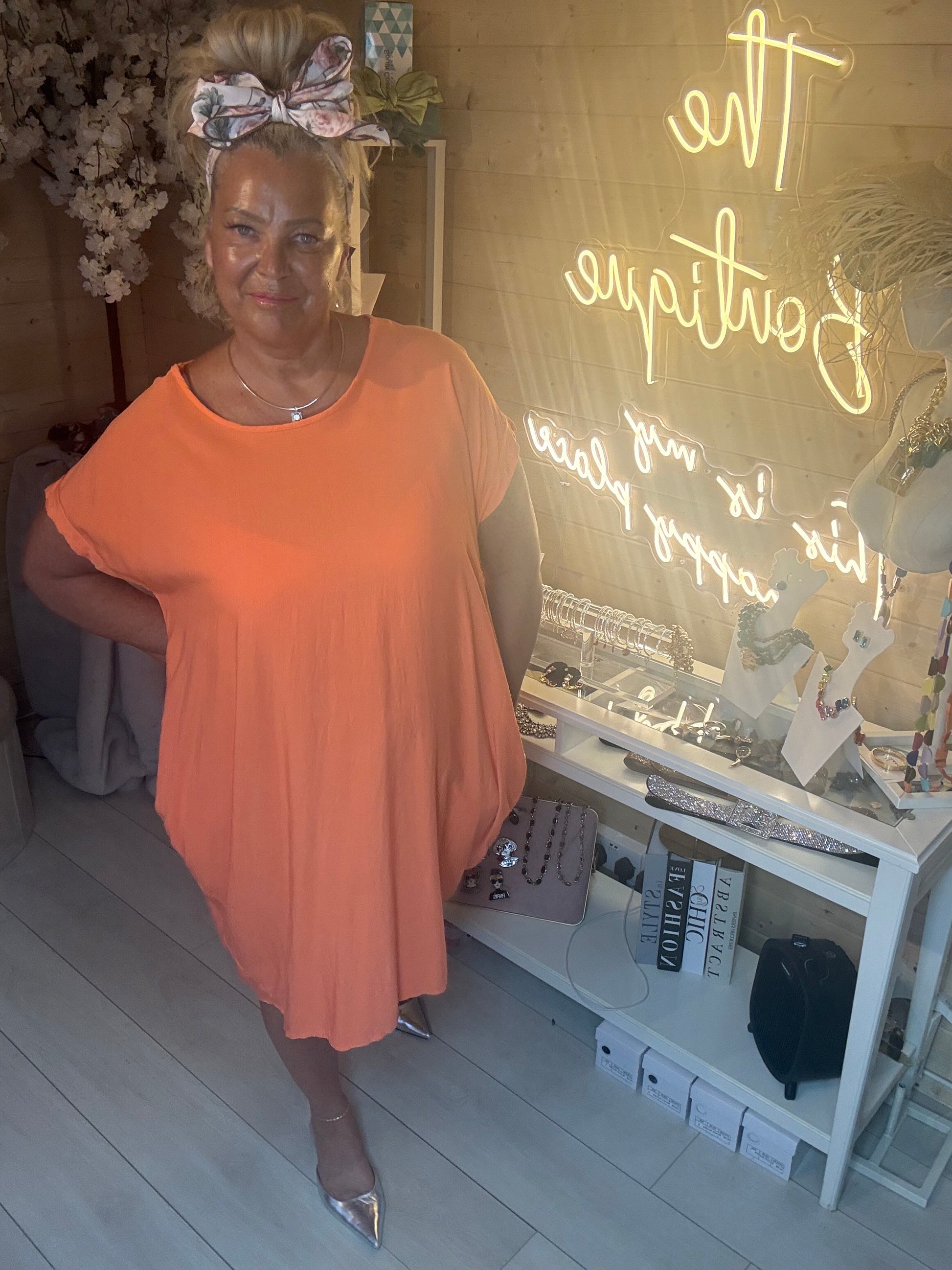 Model posing in Coral Cocoon Twist Back Jersey Dress showing relaxed cocoon silhouette and warm coral orange colour with silver heels