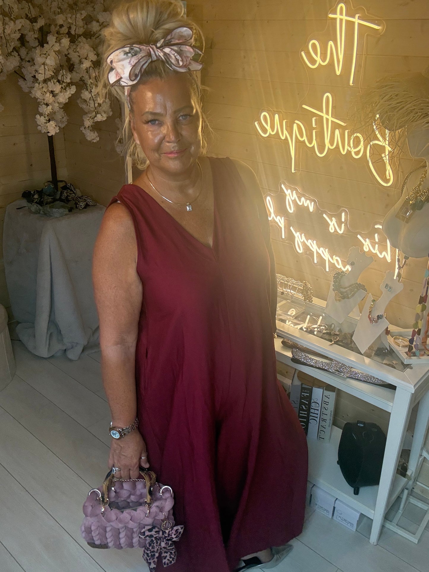 Model wearing Merlot Burgundy Sleeveless V-Neck Jumpsuit showing relaxed wide leg silhouette and deep V-neckline with lilac woven bag