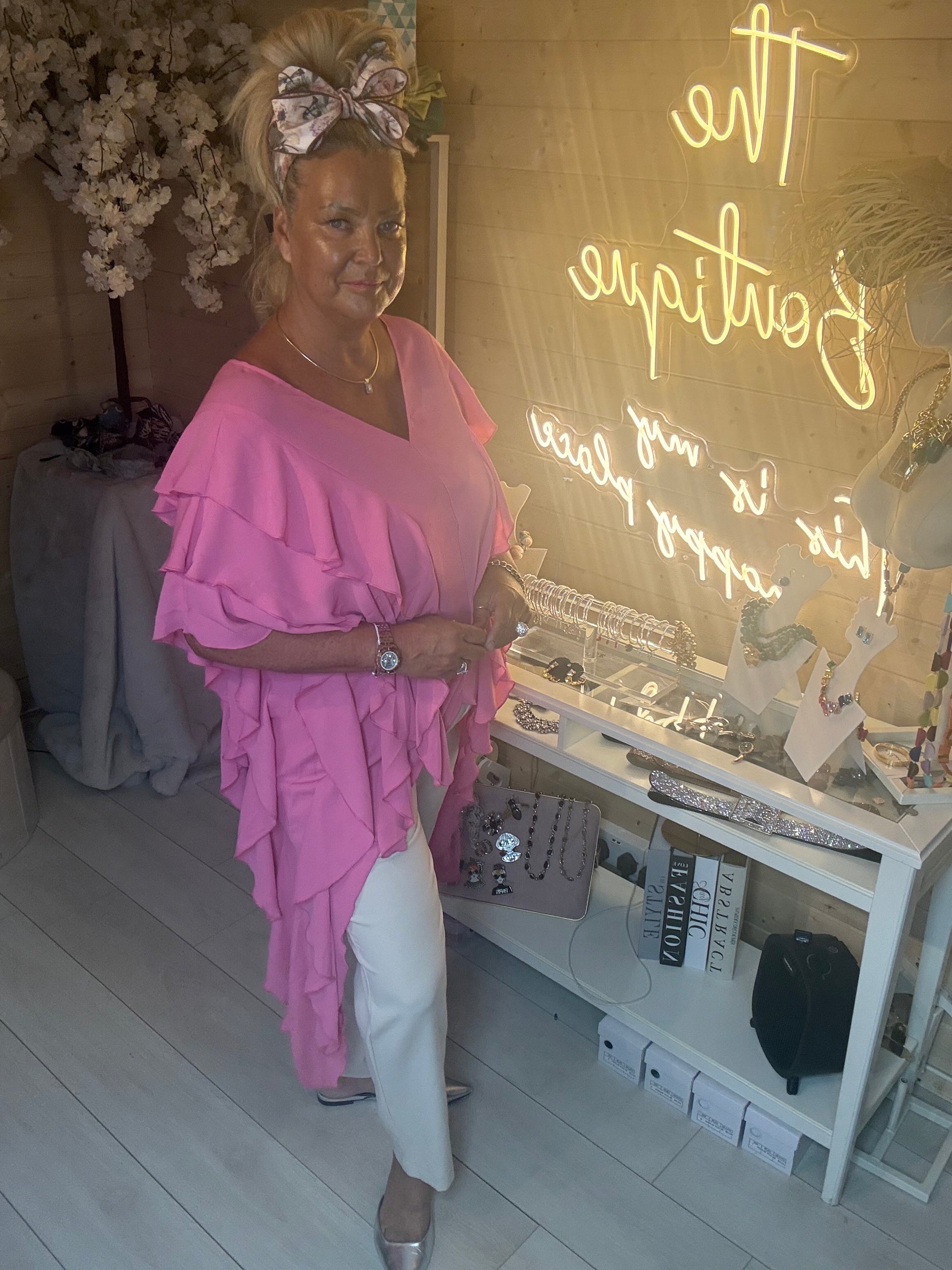 Woman wearing Fiesta Hot Pink Tiered Ruffle Top front view with cascading ruffle layers styled with white trousers and silver heels in The Ultimate Ladies Boutique
