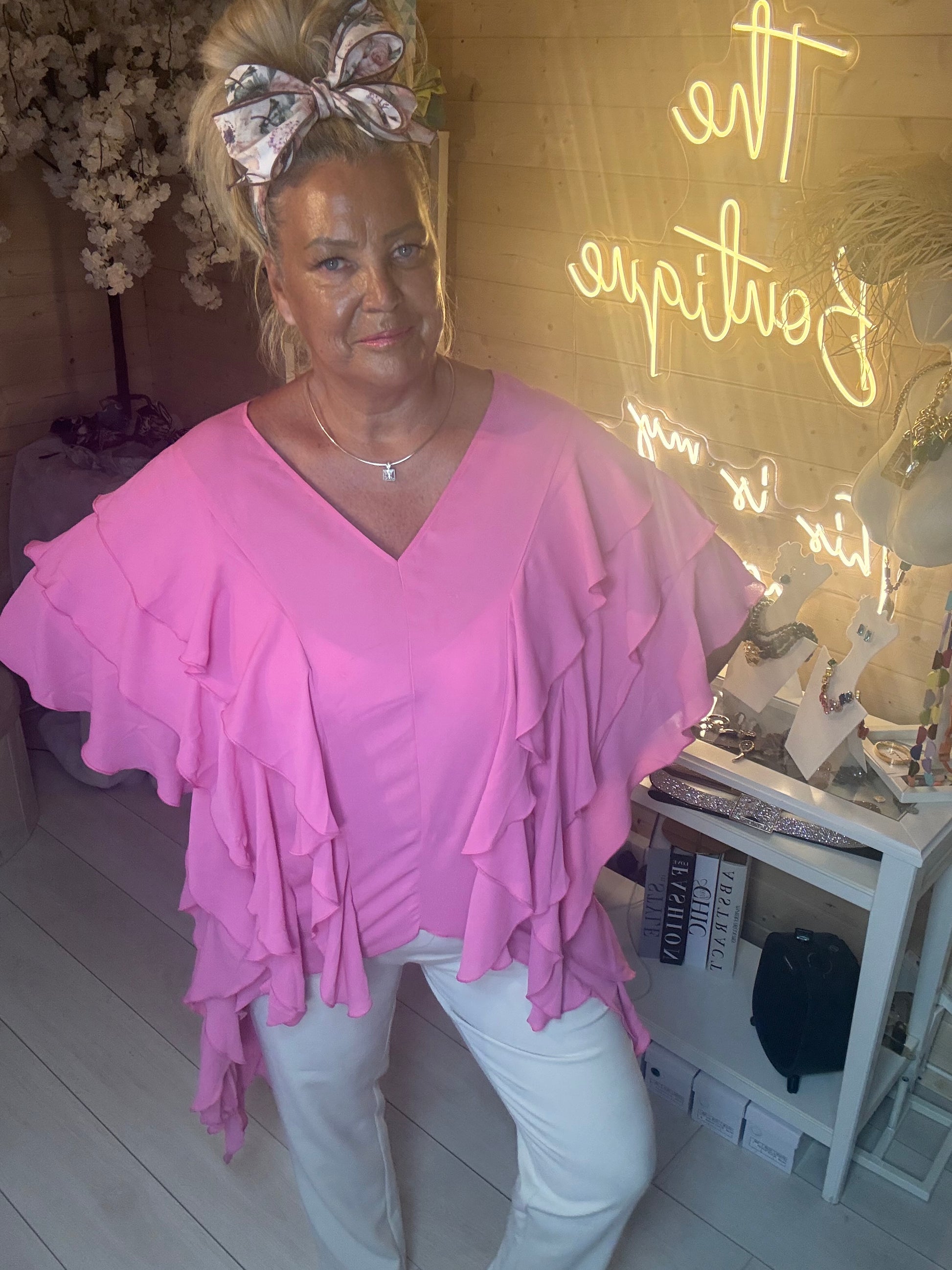Side angle view of Fiesta Hot Pink Tiered Ruffle Top showing cascading ruffle layers and relaxed fit with white trousers boutique setting
