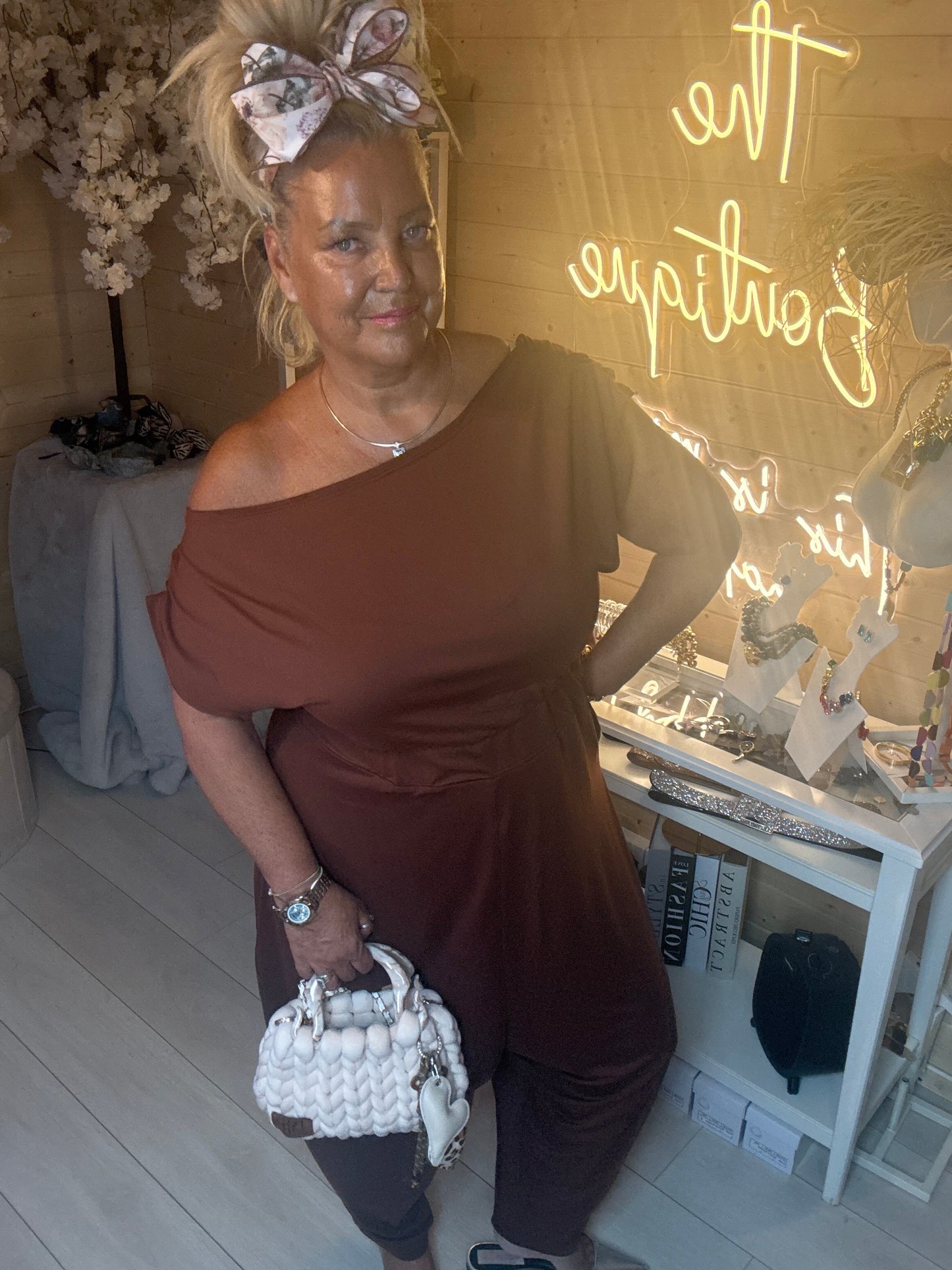 Close up of model wearing Coco Chocolate Brown Off-Shoulder Slouch Jumpsuit showing off-shoulder neckline detail and soft jersey fabric with white chunky bag