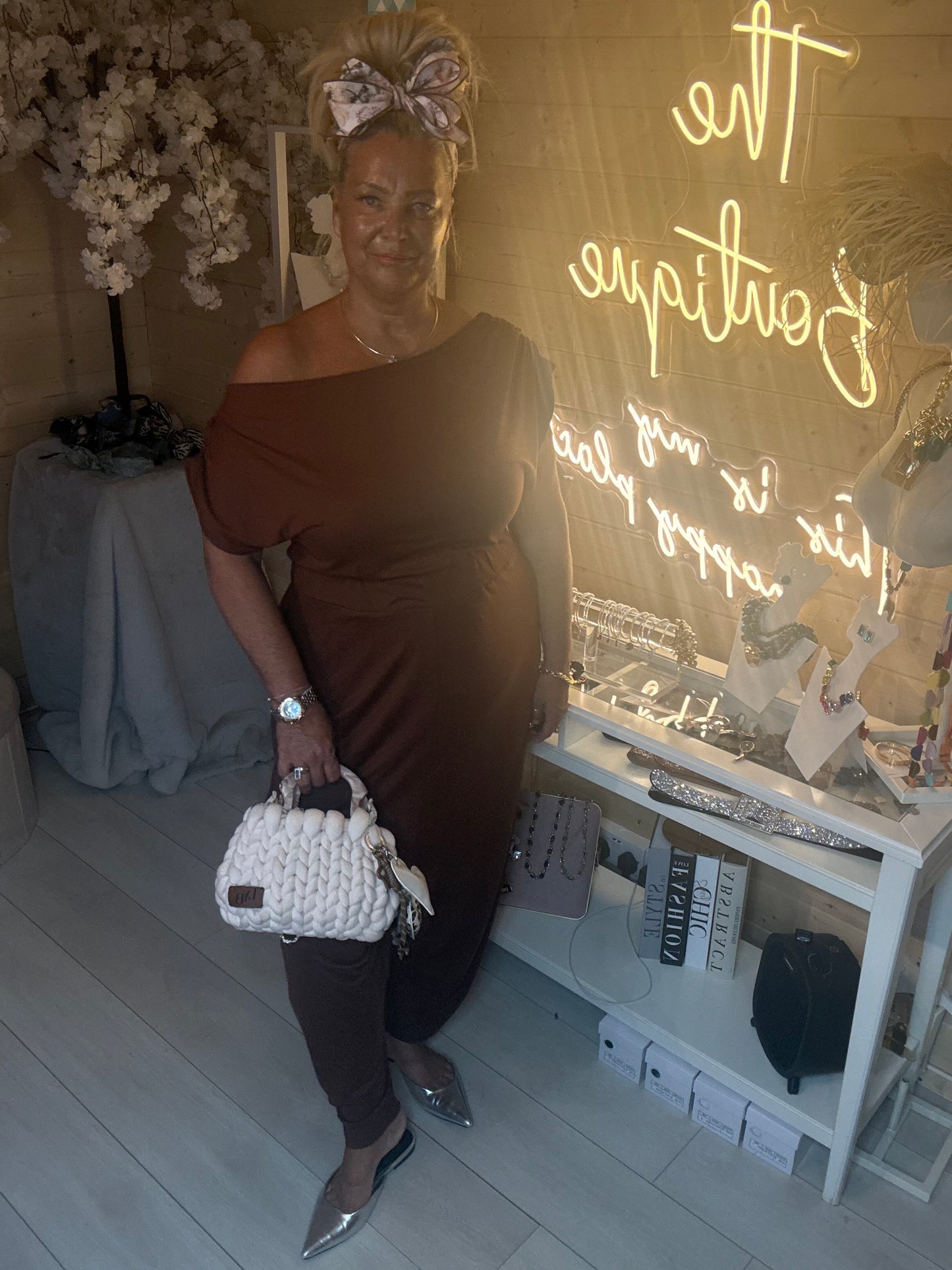 Full length view of Coco Chocolate Brown Off-Shoulder Slouch Jumpsuit with silver pointed heels and white woven mini bag showing relaxed wide leg silhouette