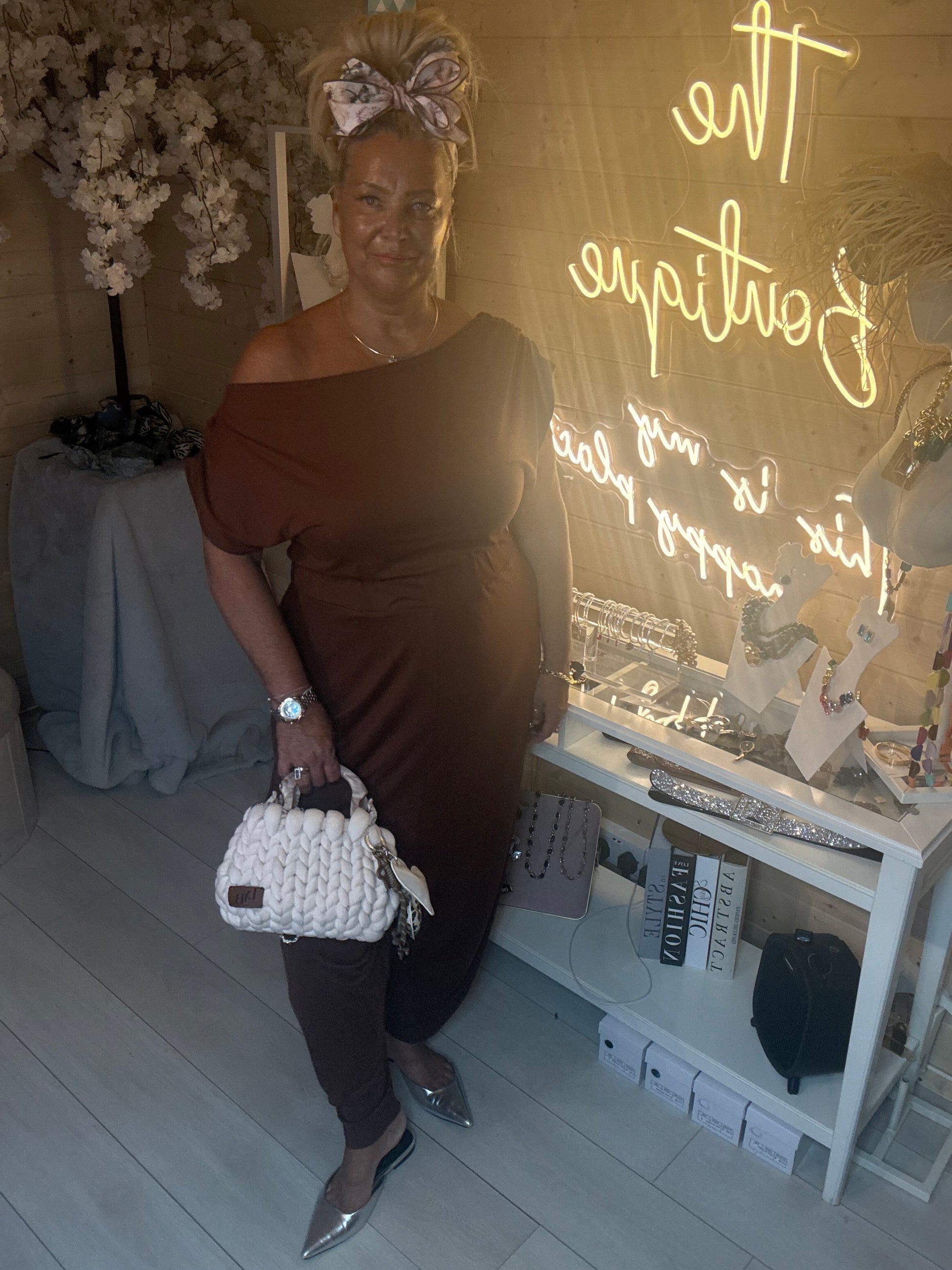 Full length view of Coco Chocolate Brown Off-Shoulder Slouch Jumpsuit with silver pointed heels and white woven mini bag showing relaxed wide leg silhouette