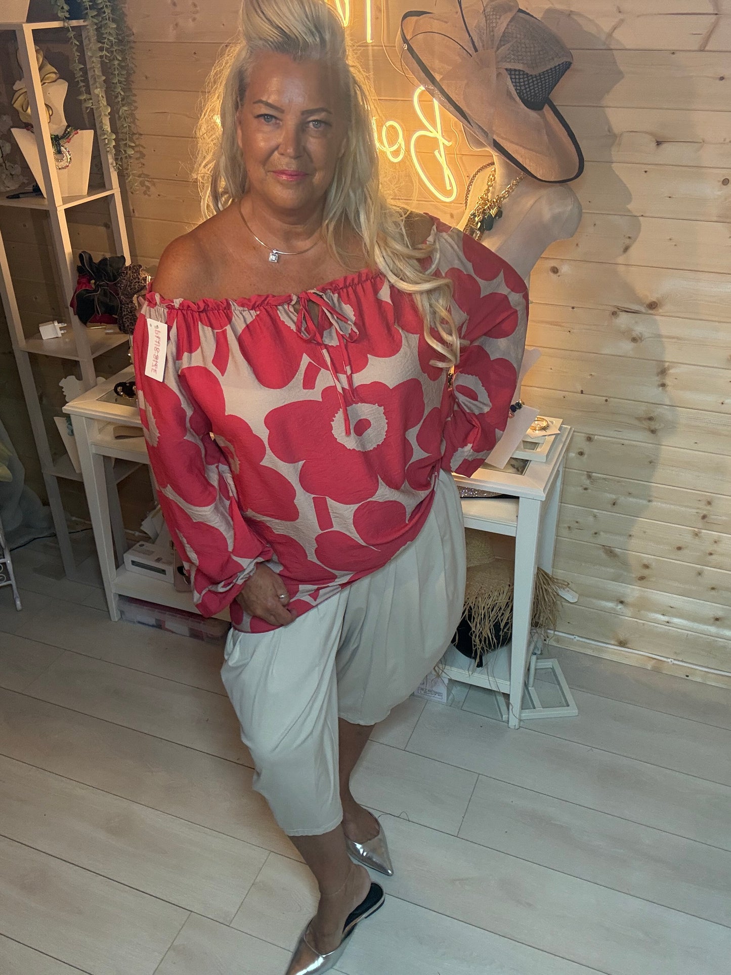 Red floral bardot off-shoulder top – styled with grey trousers and silver mules, boutique setting