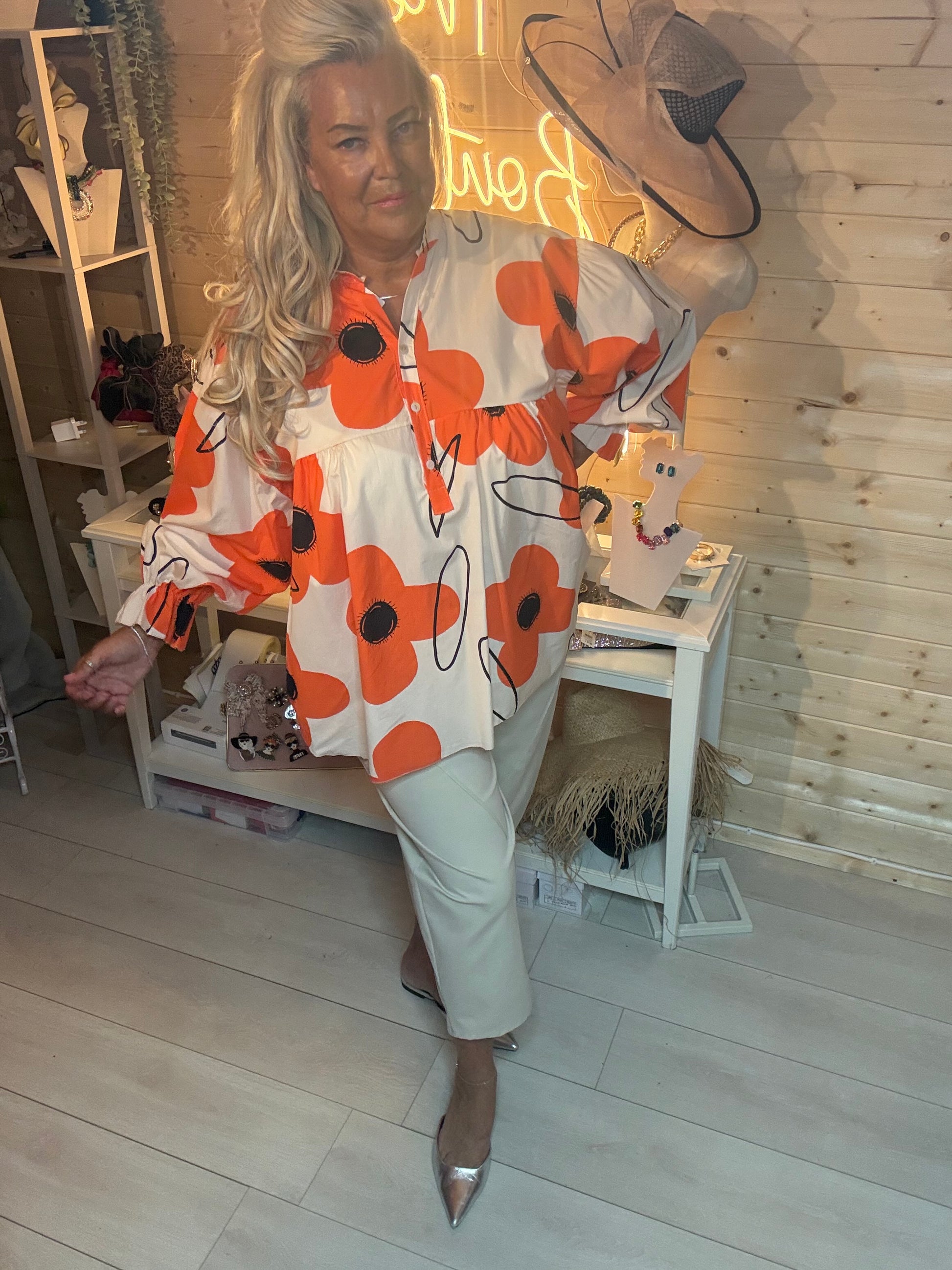 Oversized orange and white bold floral button blouse – front view showing gathered waist and fluted cuffs, styled with grey trousers and silver mules