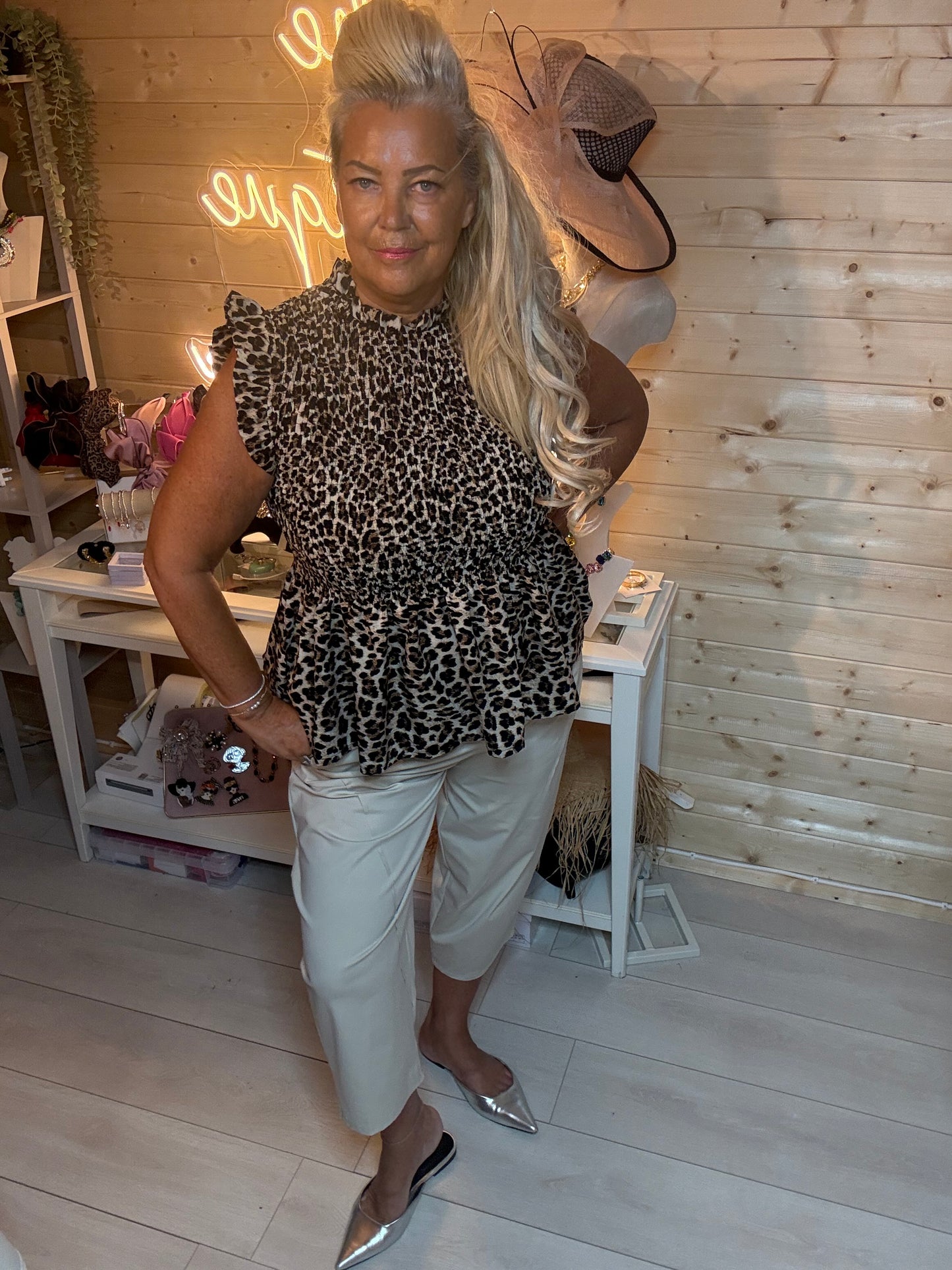 Leopard print smocked peplum top with high neck and frill cap sleeves – styled with stone cropped carrot trousers and silver mules, boutique setting