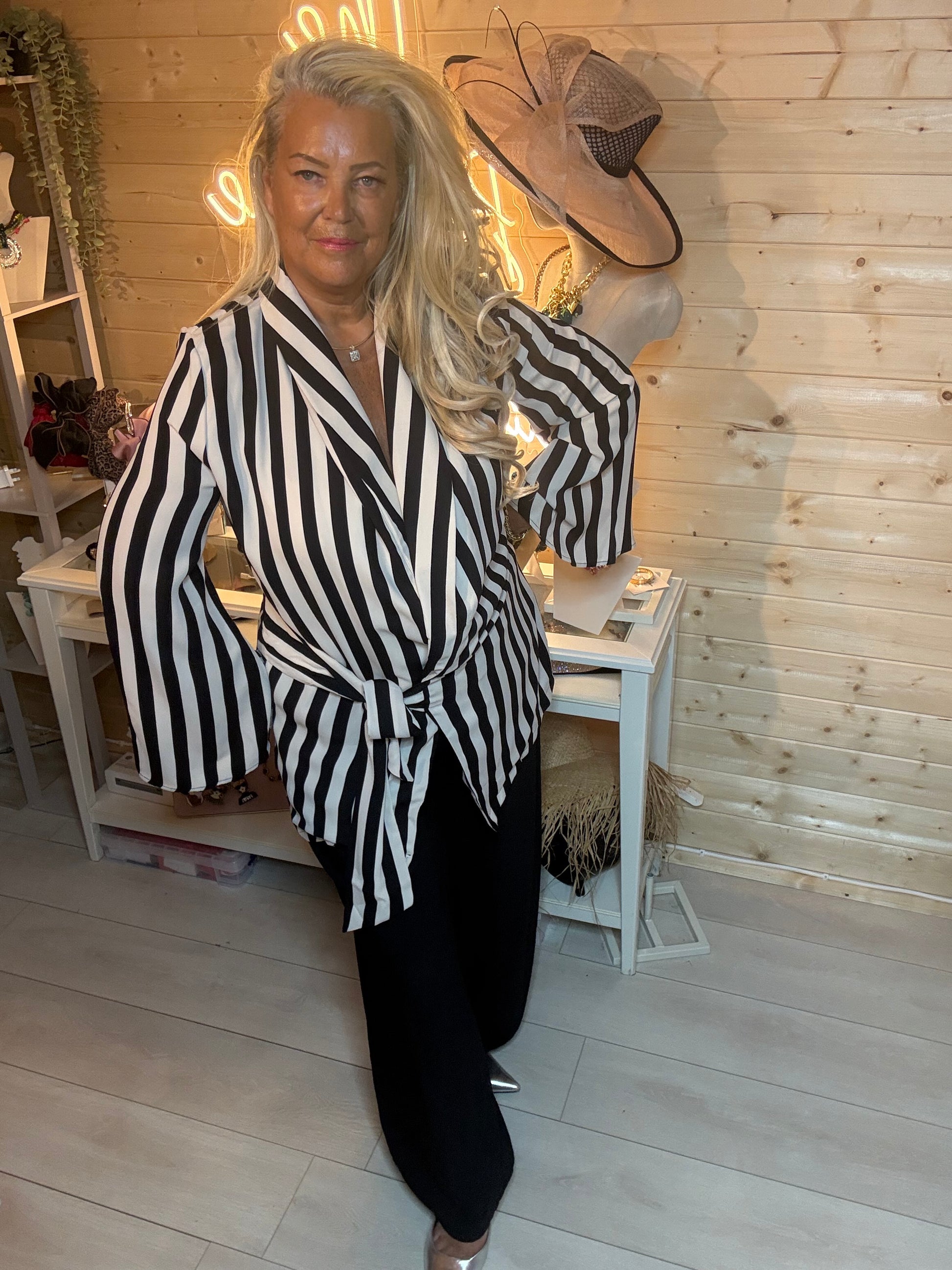 Black and cream stripe wrap jacket – three quarter view showing full silhouette with black trousers and silver mules, boutique setting