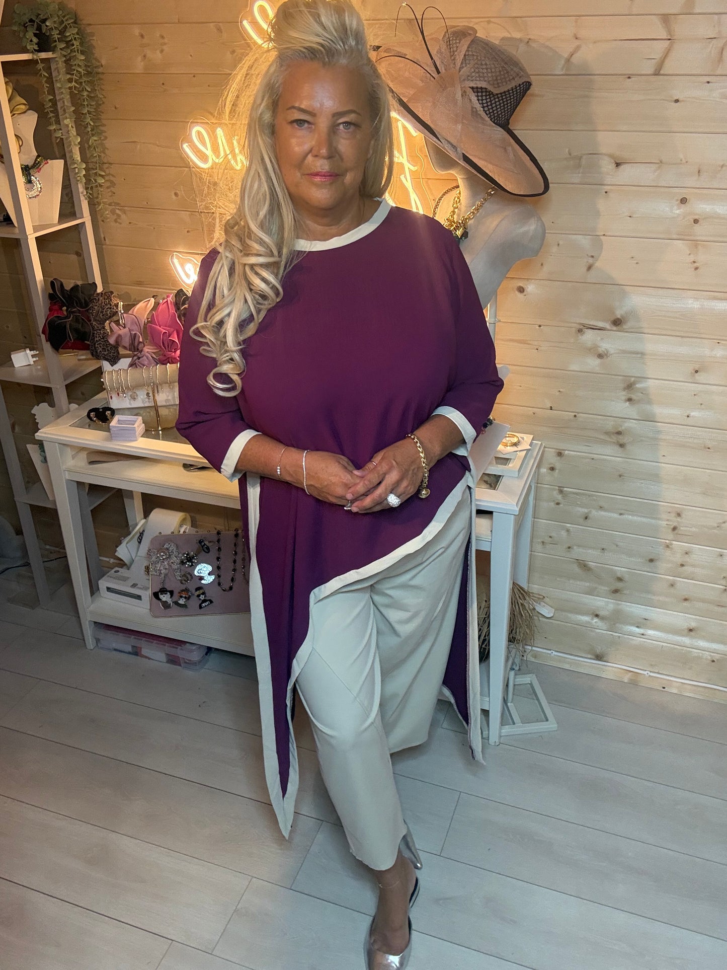 Plum asymmetric top with white contrast trim – three quarter view showing relaxed oversized fit and diagonal hem detail styled with grey trousers