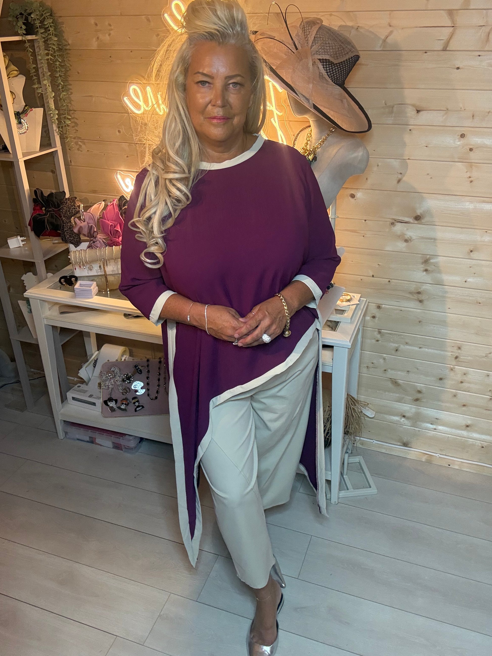 Plum asymmetric top with white contrast trim – three quarter view showing relaxed oversized fit and diagonal hem detail styled with grey trousers