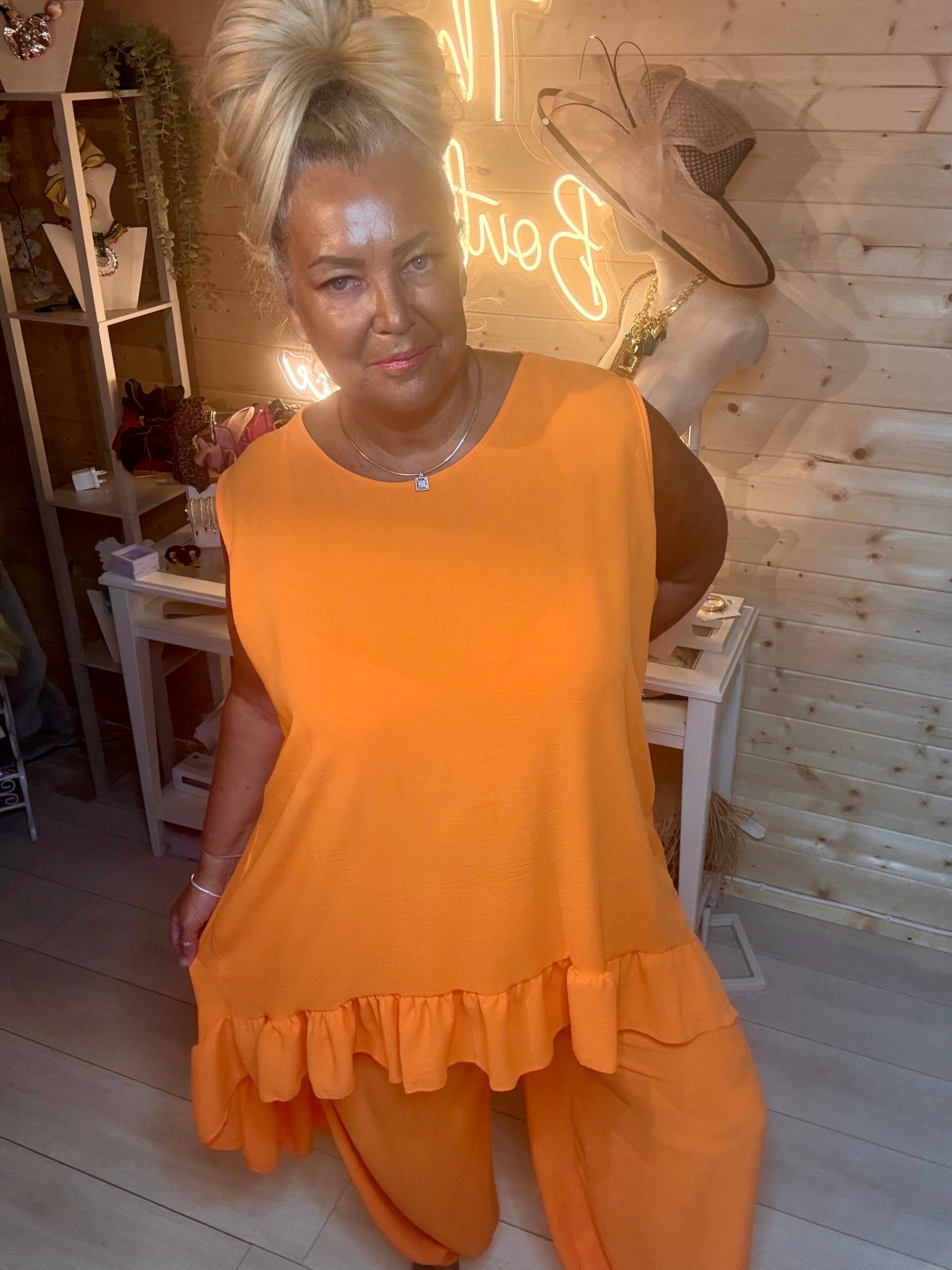 Orange ruffle hem vest top close up – showing round neckline, sleeveless design and asymmetric ruffle hem detail with matching orange trousers