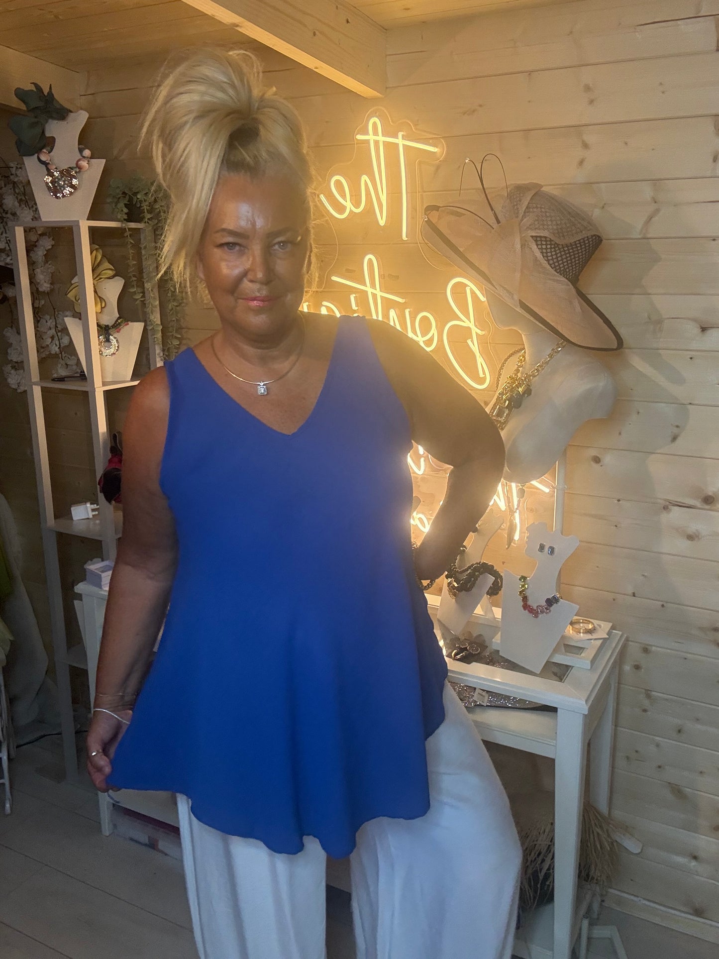Royal blue V-neck swing vest top – full length front view showing deep V-neckline and flowy swing silhouette styled with white wide-leg trousers and silver mules in boutique setting