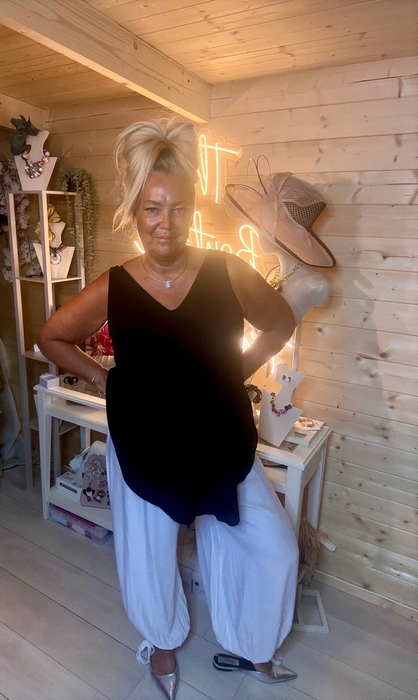 Black swing vest top – three quarter length boutique shot showing relaxed swing silhouette and asymmetric curved hem with white trousers