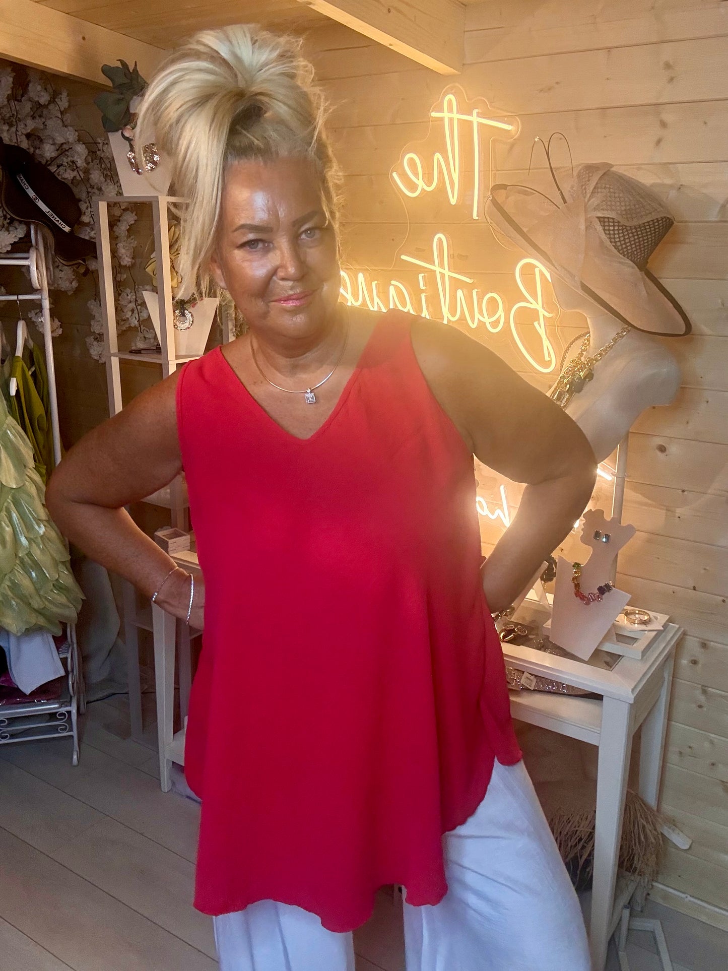 Red swing vest top – three quarter length boutique shot showing curved asymmetric hem and relaxed silhouette in vibrant red with white trousers and silver mules