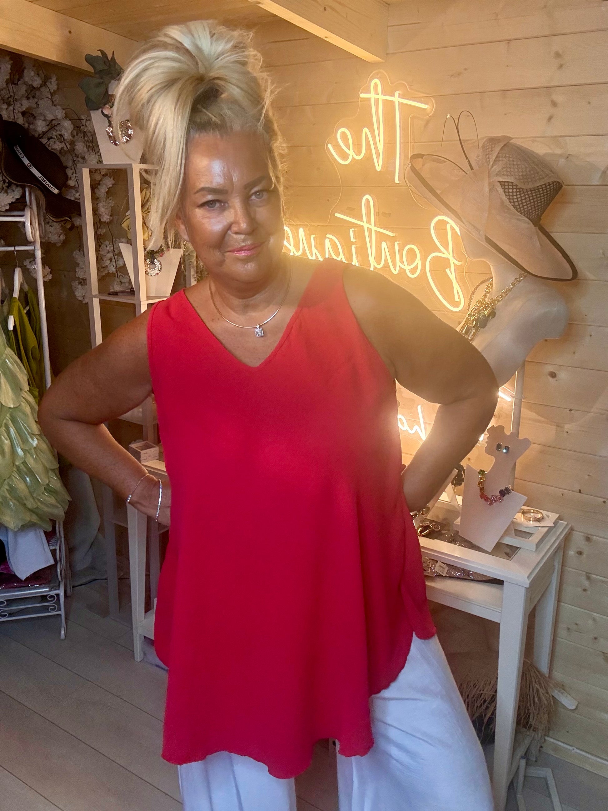Red swing vest top – three quarter length boutique shot showing curved asymmetric hem and relaxed silhouette in vibrant red with white trousers and silver mules