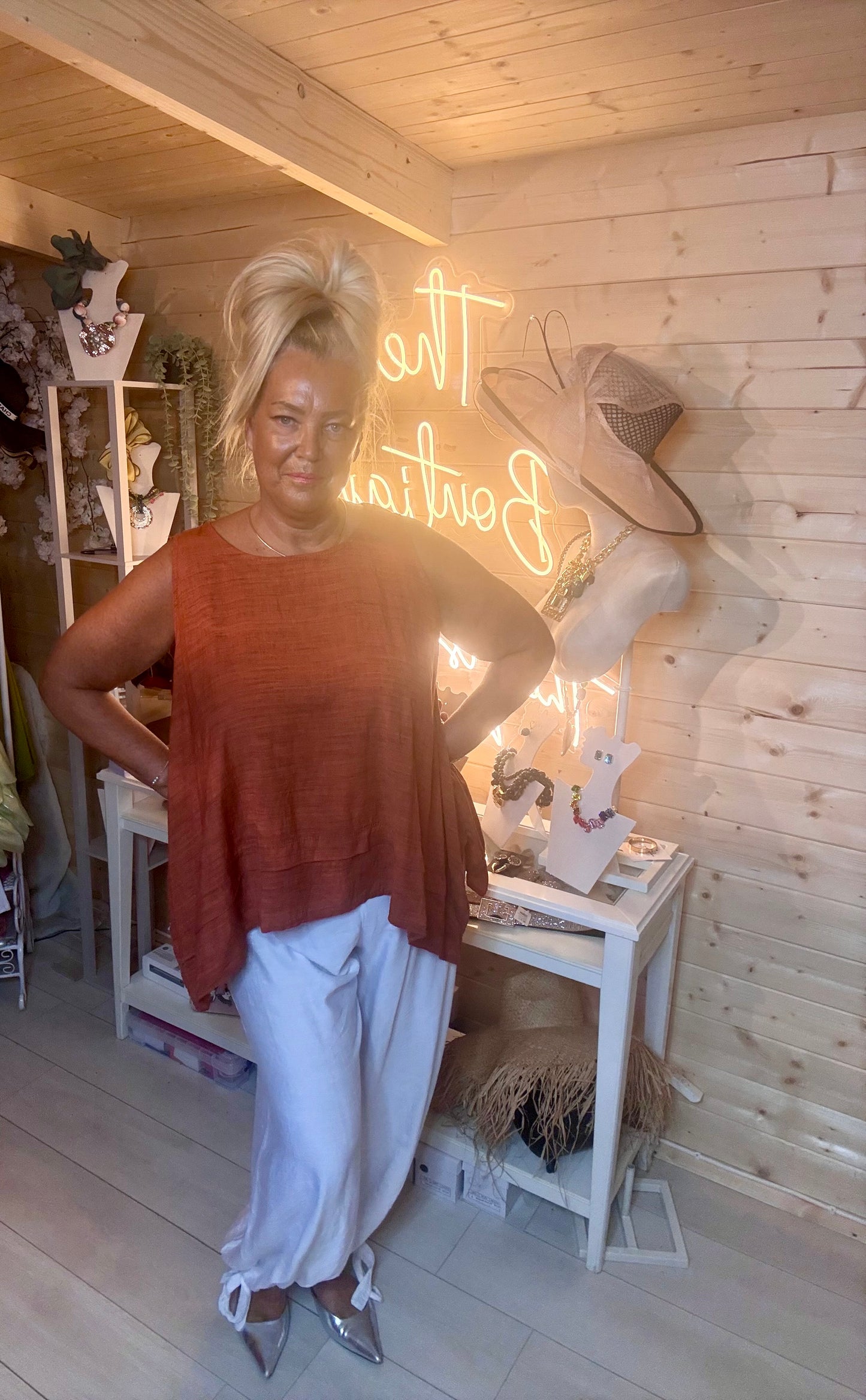 Rust terracotta swing top – full length side view showing longer back hem detail and relaxed silhouette styled with white wide-leg trousers and silver mules