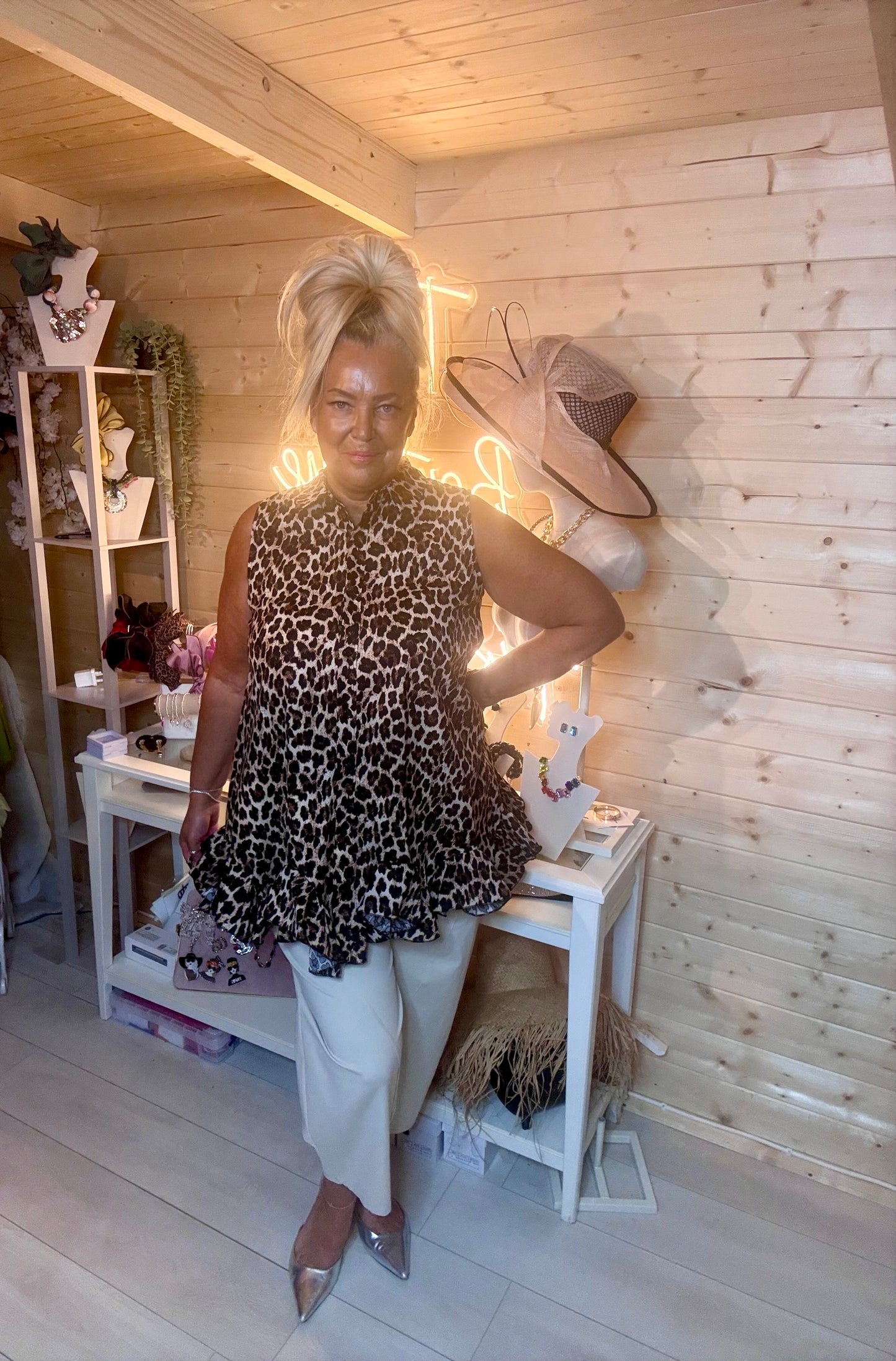 Leopard print swing tunic top – full length front view showing shirt collar, button placket and tiered peplum ruffle hem styled with white wide-leg trousers and silver mules in boutique setting