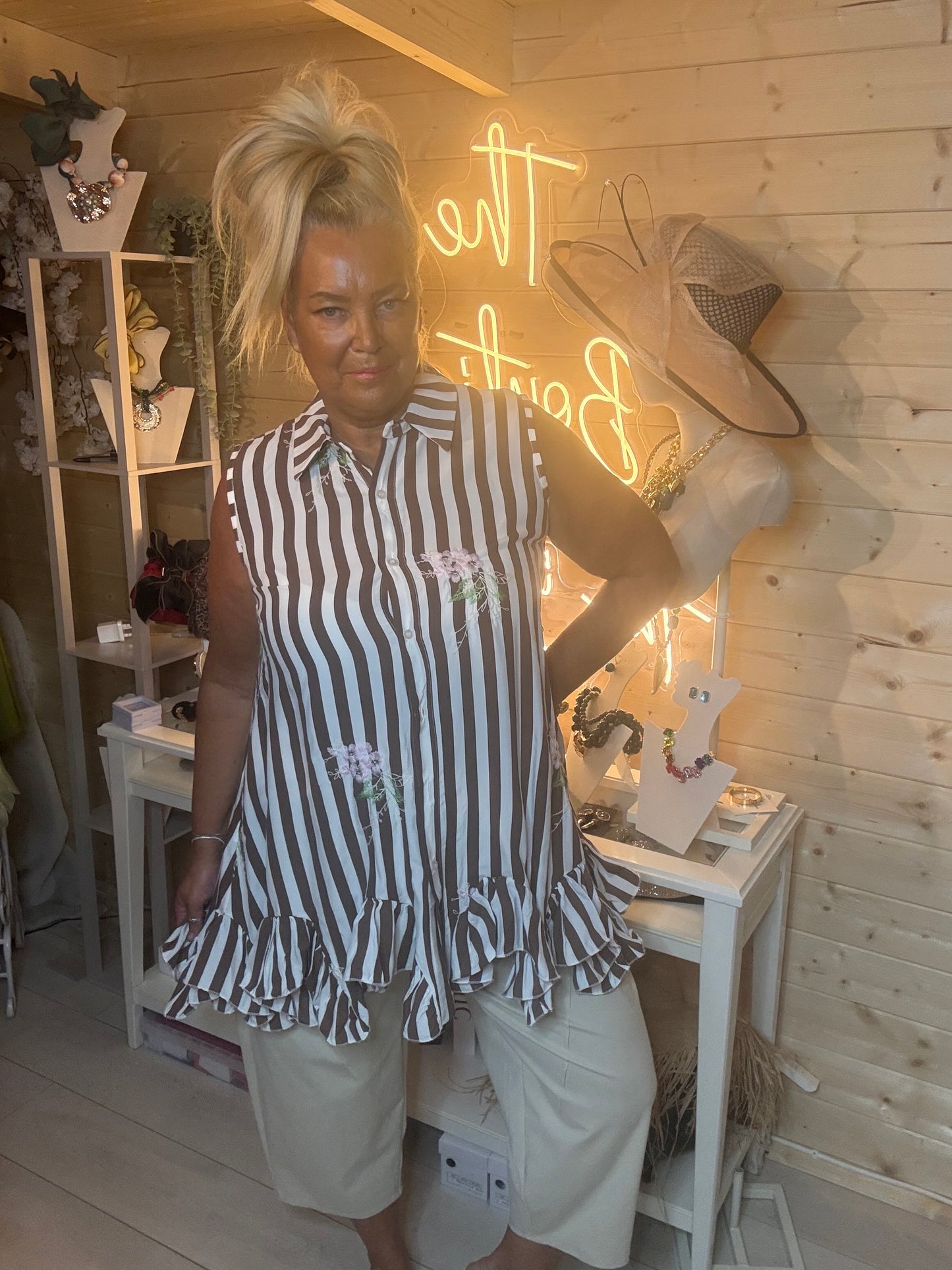 Navy and white stripe sleeveless shirt tunic – full length front view showing classic collar, button placket, floral embroidery and double ruffle peplum hem styled with white trousers in boutique setting
