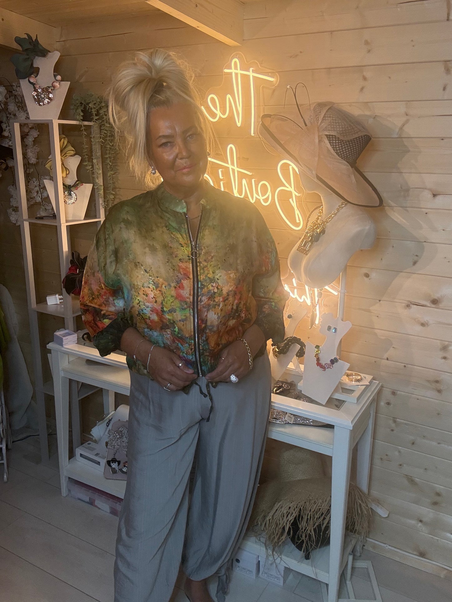 Floral bomber jacket – full length three quarter view showing relaxed batwing silhouette and elasticated hem styled with grey wide-leg trousers and silver mules