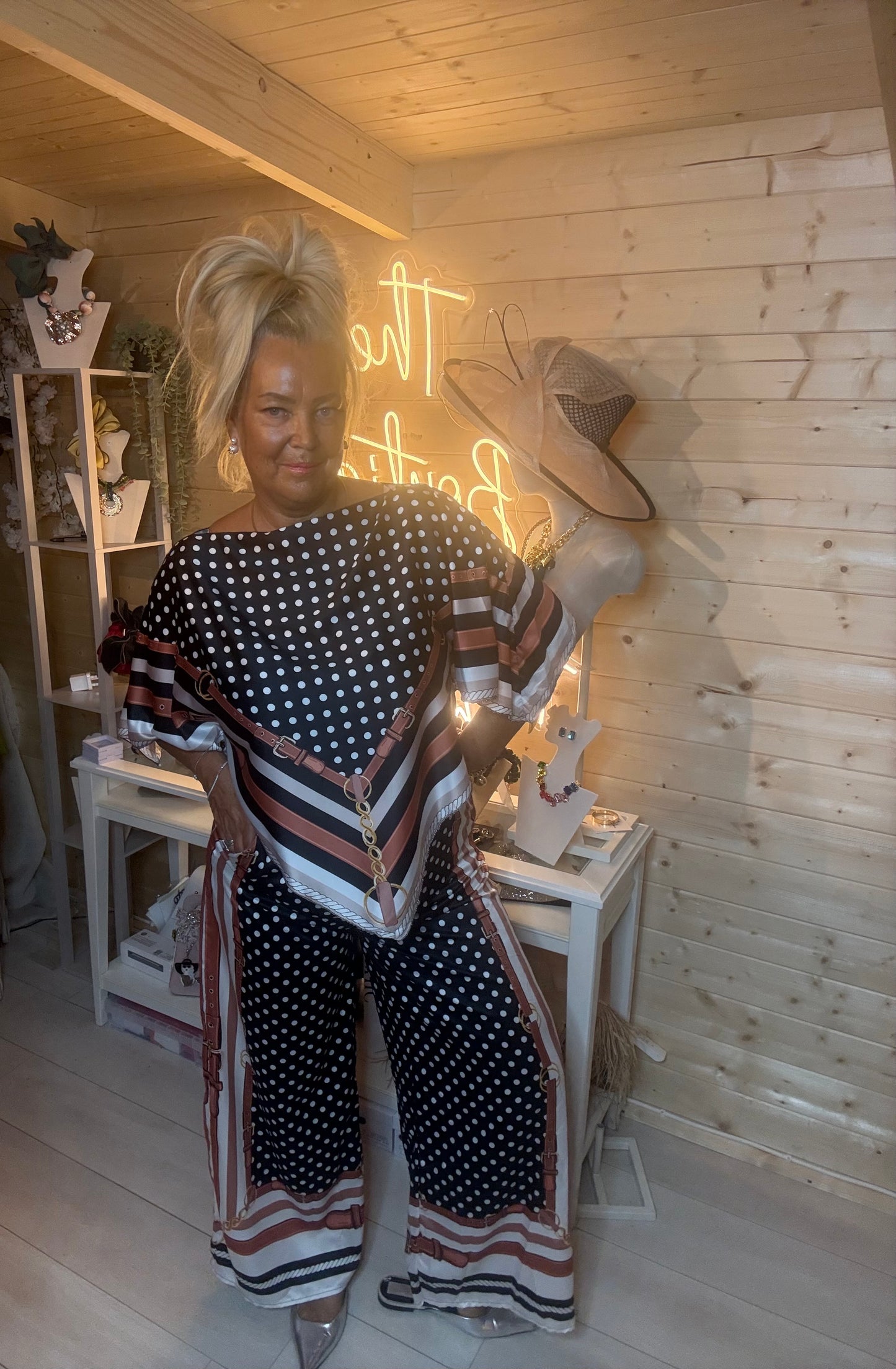 Black polka dot scarf print co-ord set – full length front view showing batwing top with chevron scarf-print hem and matching wide-leg trousers styled with silver mules in boutique setting